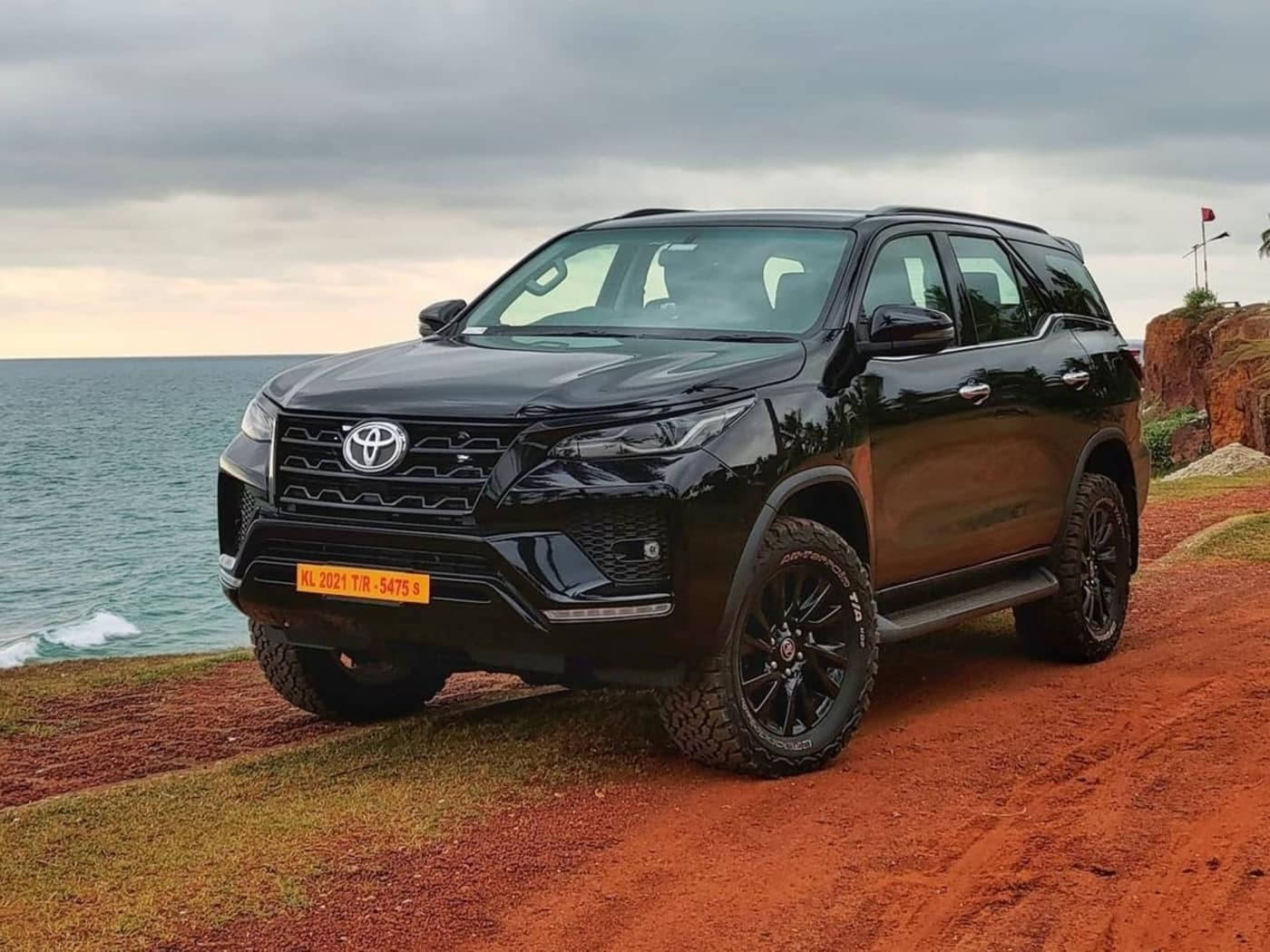 Toyota 桌布 壁紙 — 一輛亮黑色豐田 Fortuner SUV 停泊在紅土懸崖上，俯瞰多雲天空下的海洋。