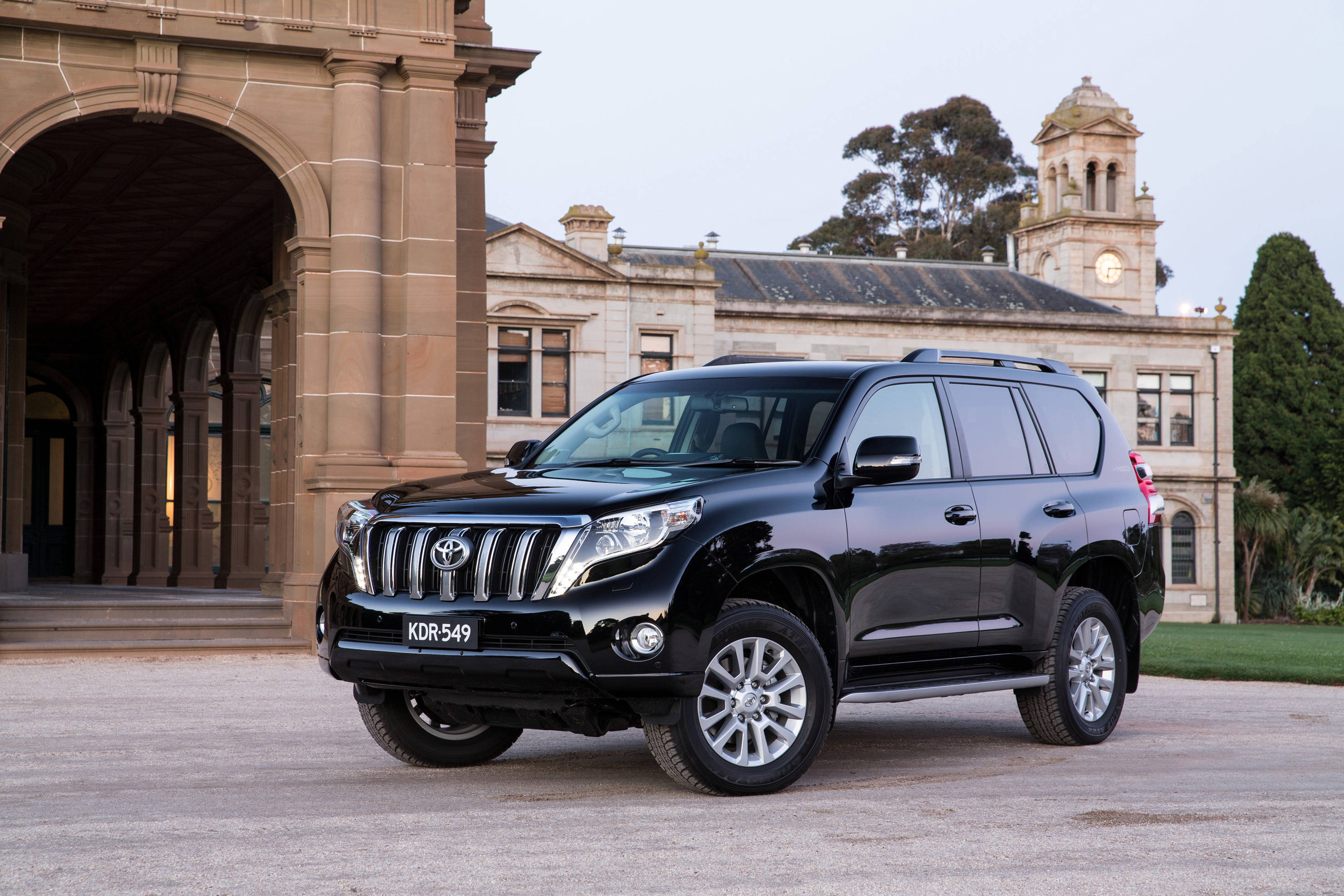 Toyota 桌布 壁紙 — 一輛亮黑色豐田Land Cruiser SUV停在一座帶有拱形柱廊和鐘樓的宏偉石建築前。