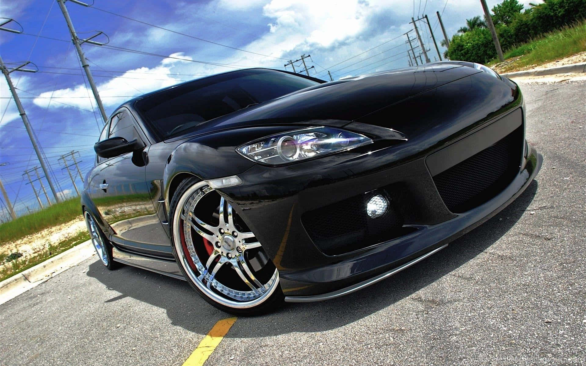 Mazda Rx-8 桌布 壁紙 — 一輛亮黑色跑車配備定制鍍鉻輪圈，停在瀝青路上，上方是藍天白雲。
