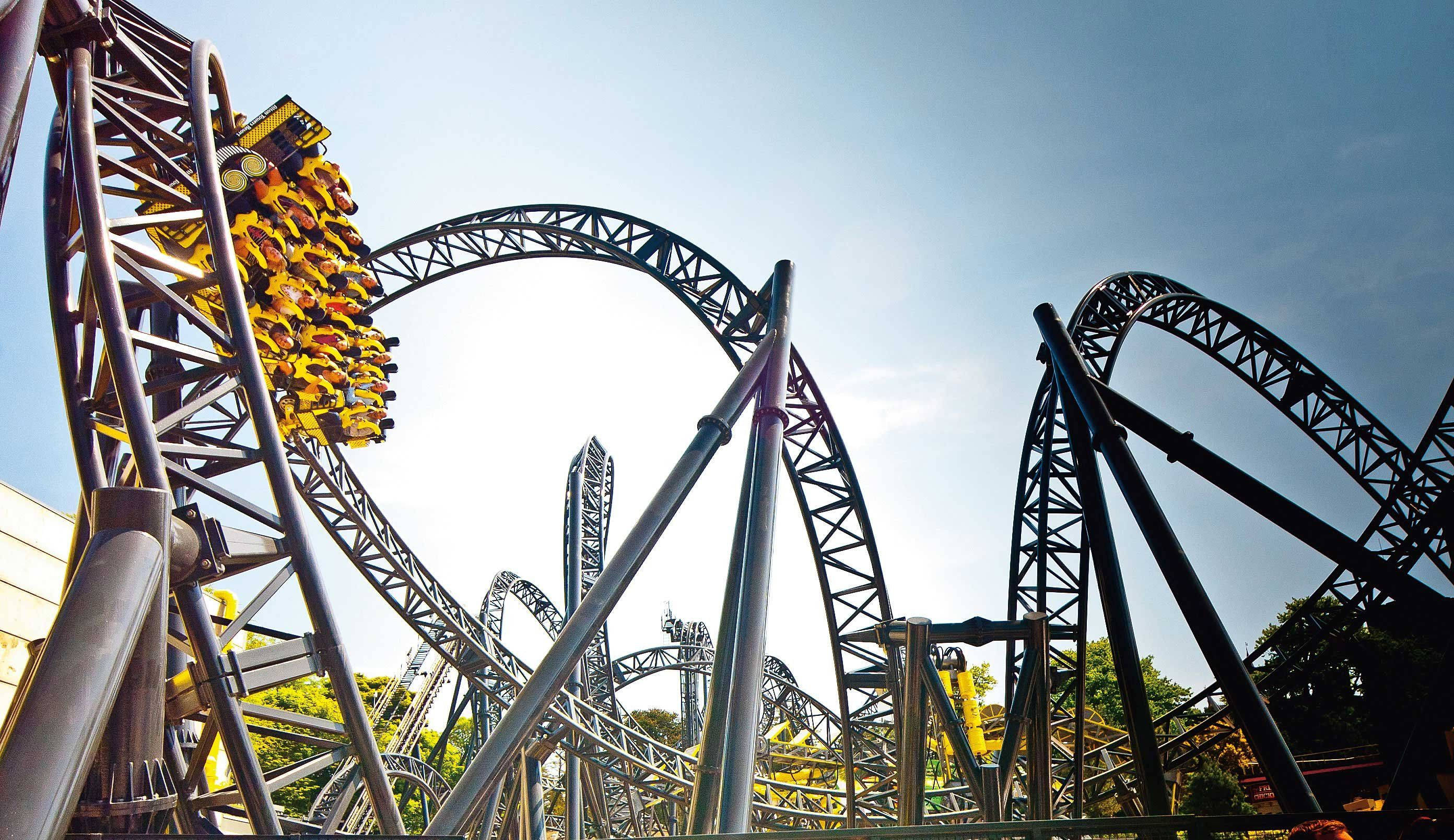 Roller Coaster 桌布 壁紙 — 一輛令人興奮的黃色雲霄飛車在晴朗的藍天下飛馳穿過高聳的鋼製環圈。