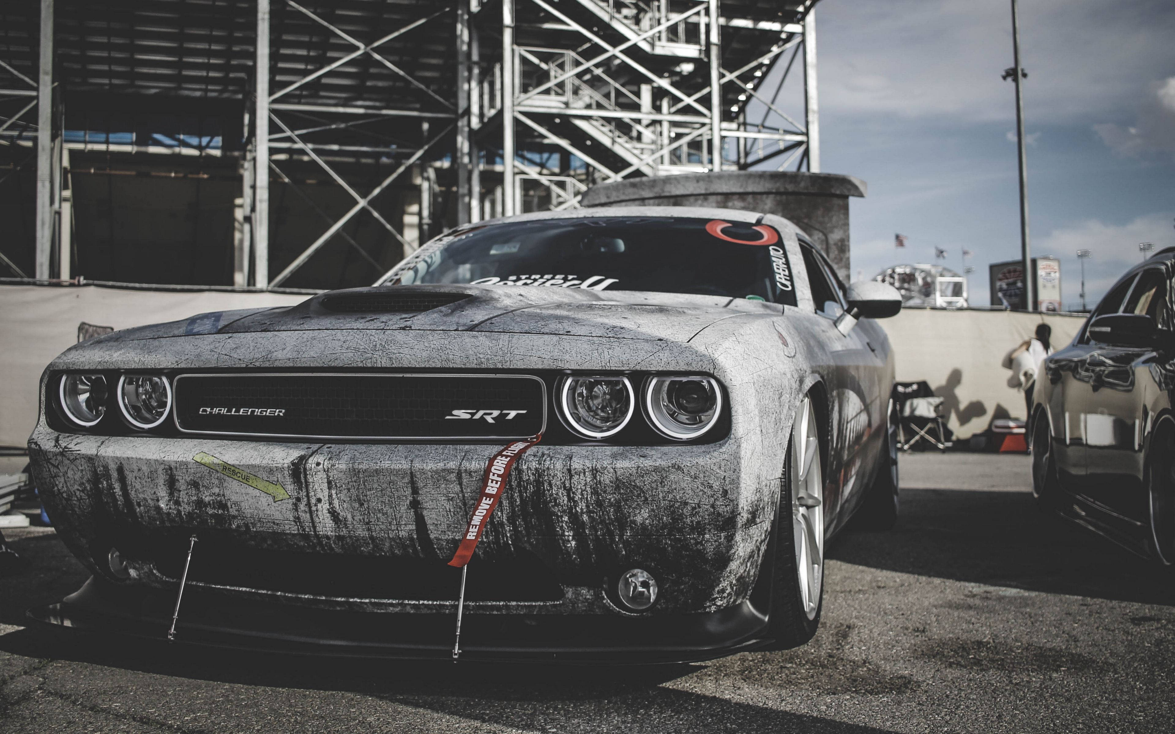 Challenger 桌布 壁紙 — 一輛佈滿灰塵的灰色 Dodge Challenger SRT 停在賽車場上，背景有金屬鷹架，天空晴朗。
