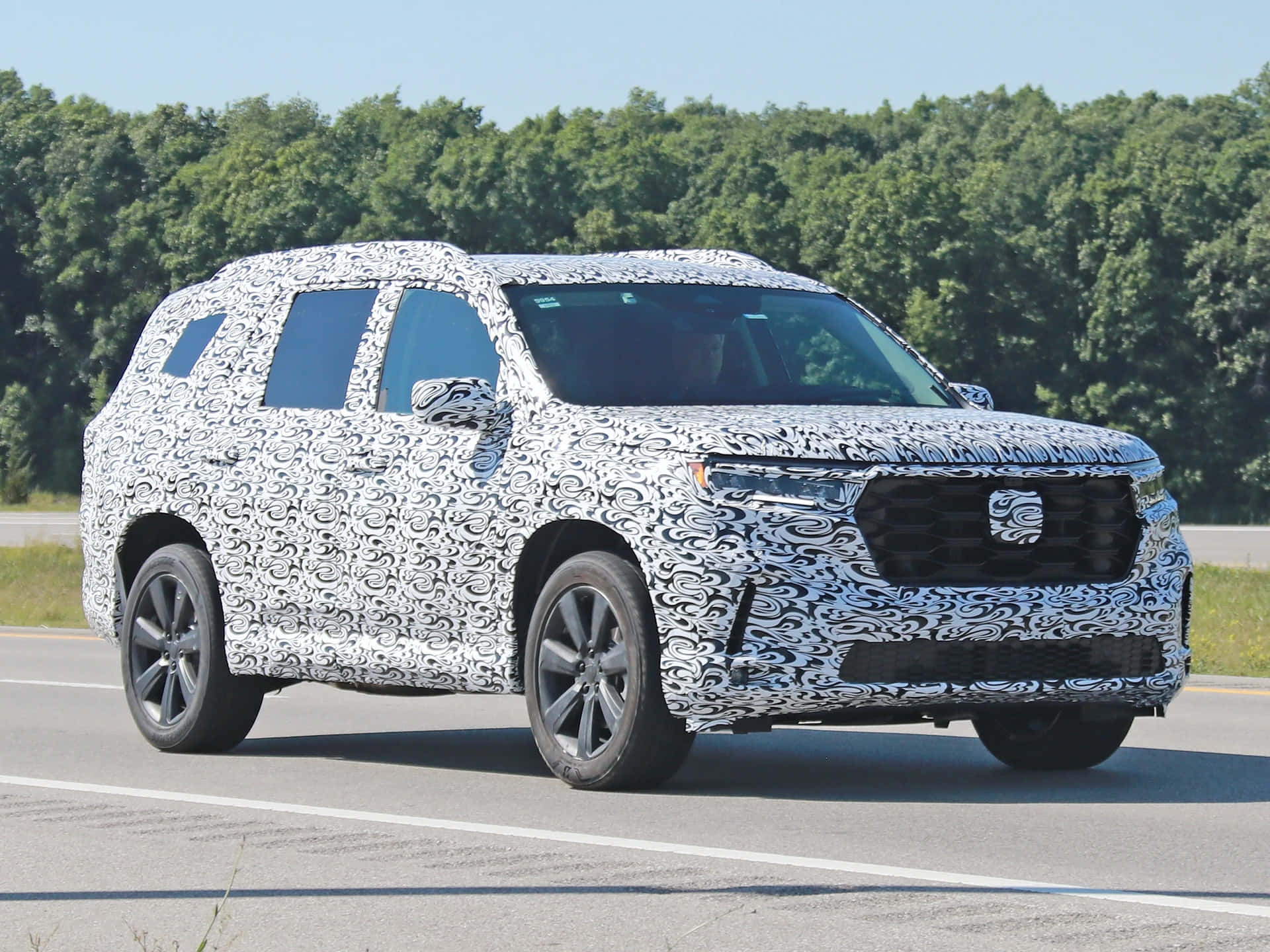 Honda Pilot 桌布 壁紙 — 一輛偽裝的SUV原型車在陽光明媚的高速公路上行駛，背景是綠樹。