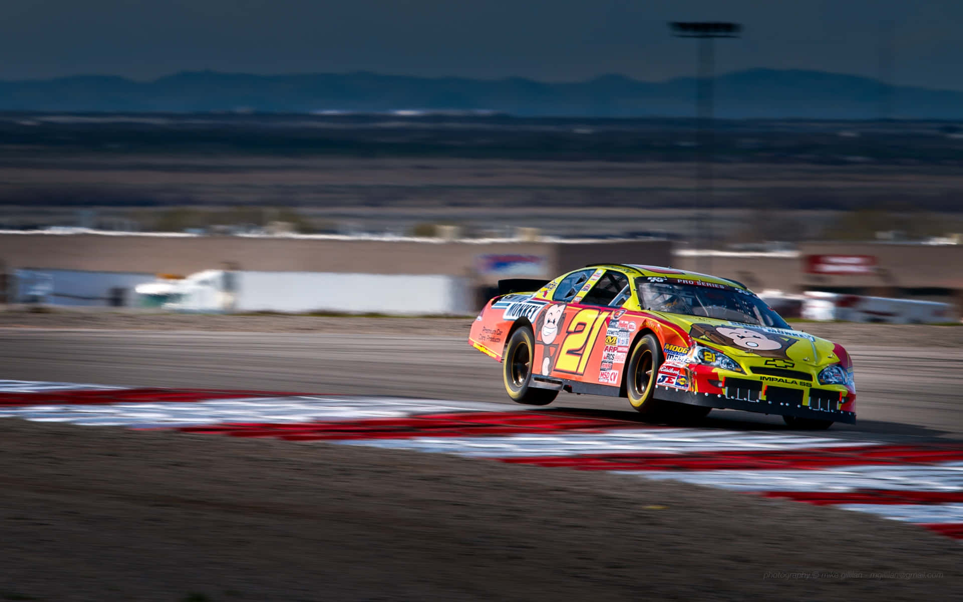 nascar 桌布 壁紙 — 一輛充滿活力的21號賽車在昏暗的天空下，沿著帶有紅色和白色路緣的賽道疾馳。