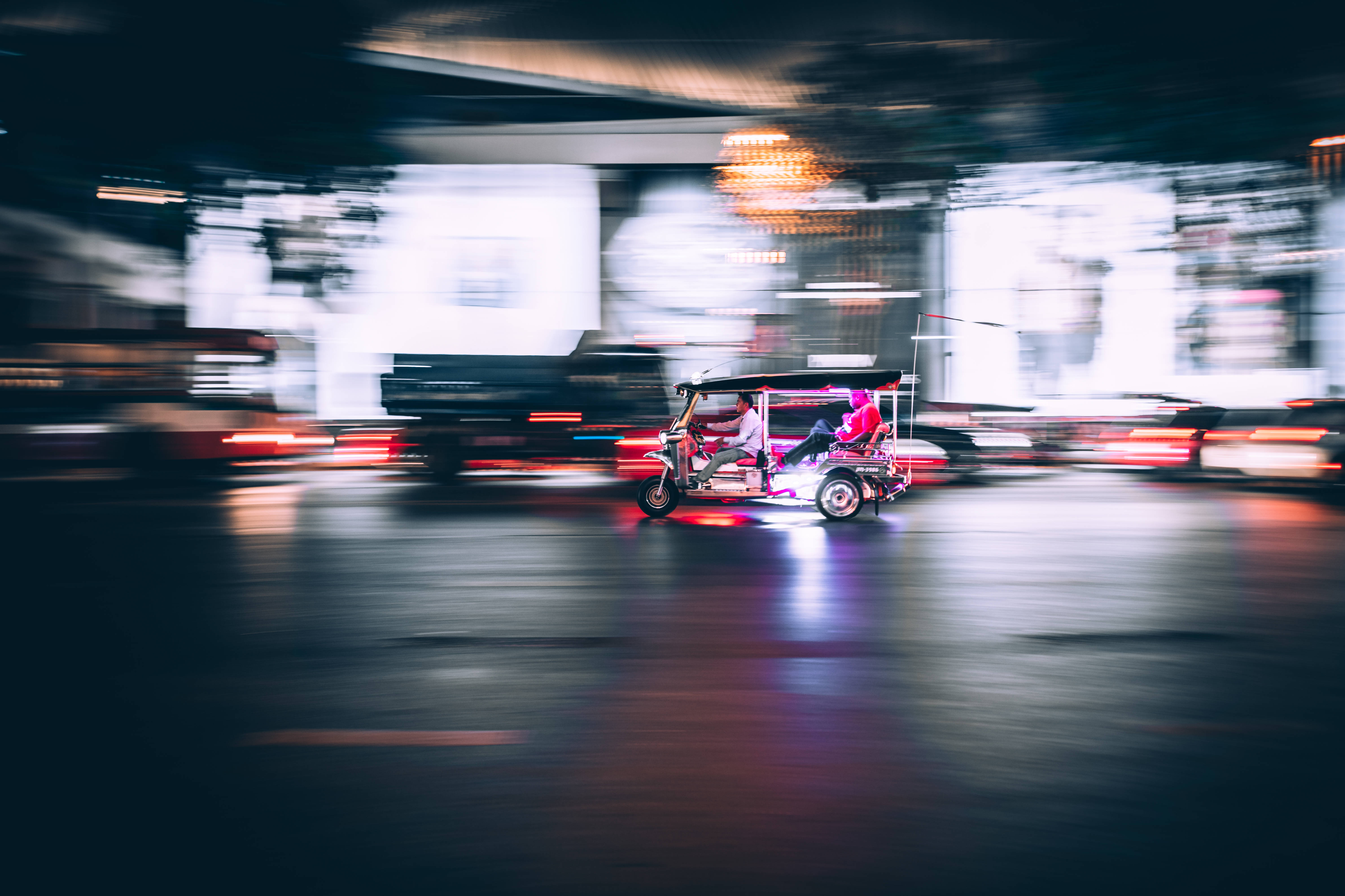 sad iPhone 桌布 壁紙 — 一輛充滿活力的嘟嘟車在模糊的夜景中疾馳，伴隨著流動的光線和發光的霓虹燈點綴。