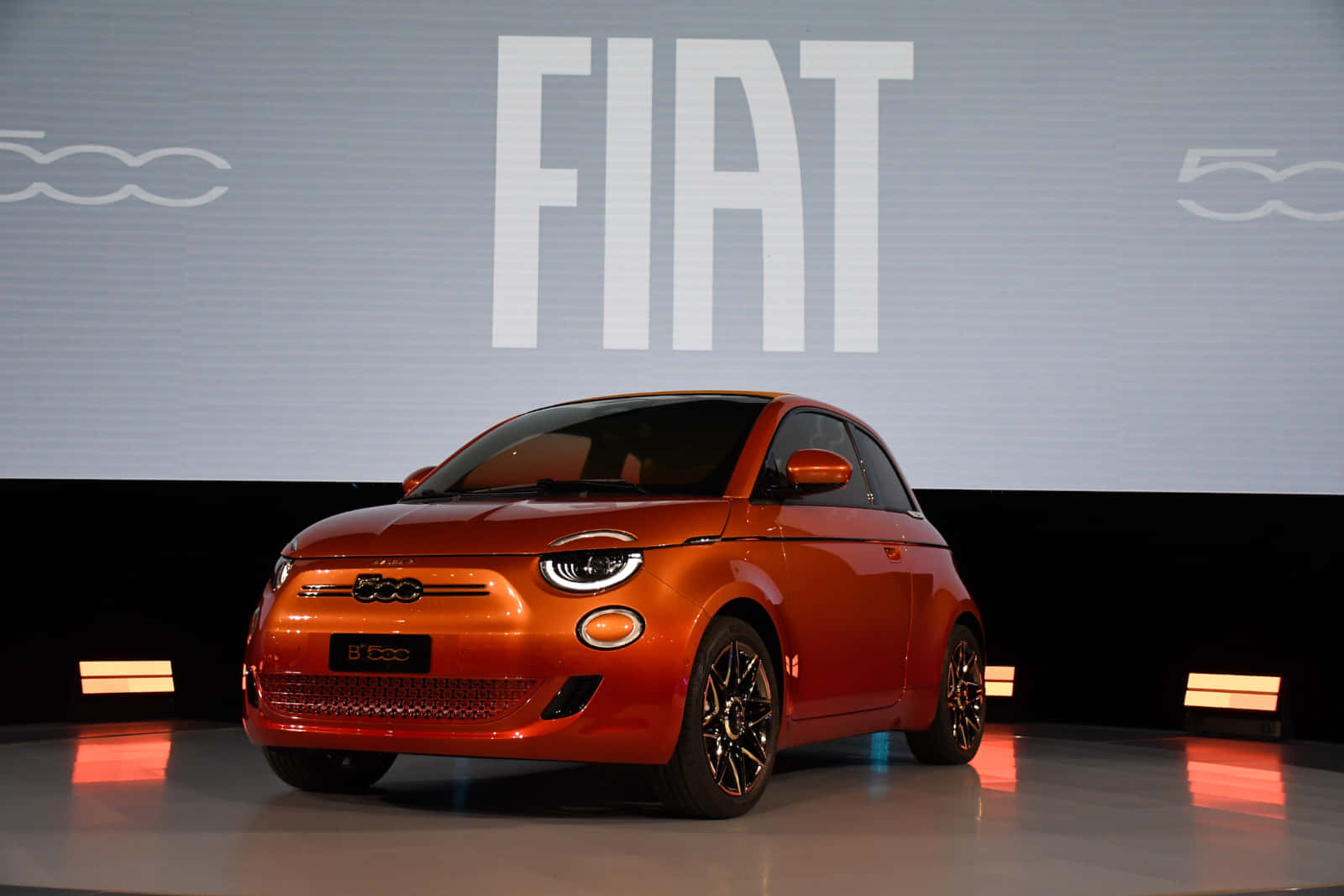 飛雅特 桌布 壁紙 — 一輛充滿活力的橘色Fiat 500e電動車在時尚的汽車發布活動中，在舞台燈光下閃閃發光。