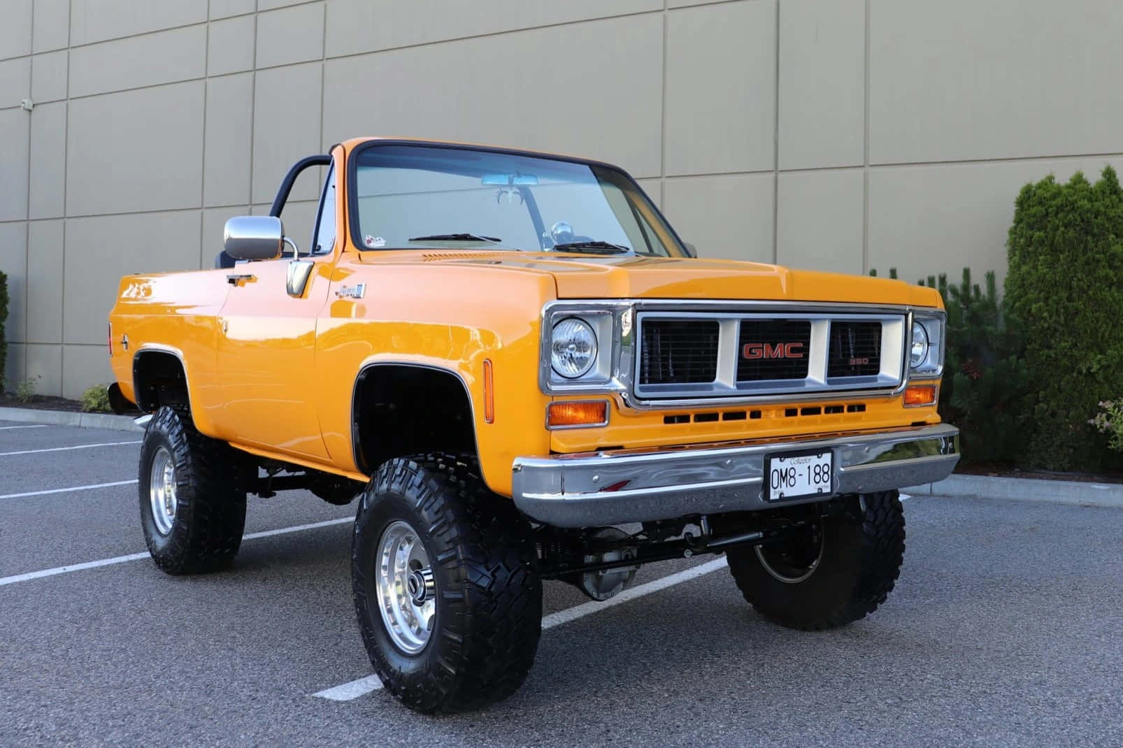 Gmc Jimmy 桌布 壁紙 — 一輛充滿活力的橘色升高GMC皮卡車，帶有鍍鉻裝飾和大輪胎，停在現代化的停車場中。