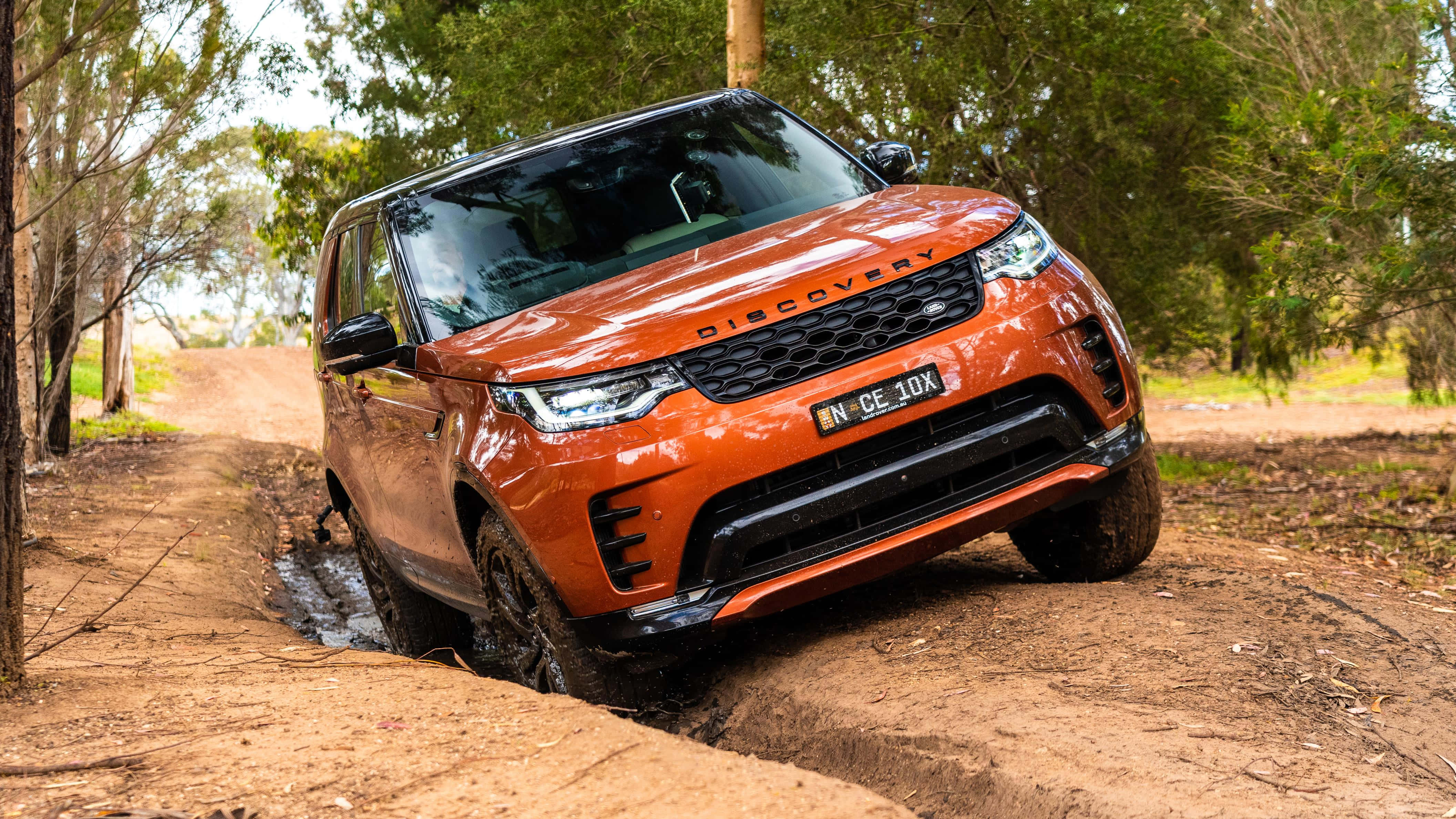 Land Rover Discovery 桌布 壁紙 — 一輛充滿活力的橙色 Land Rover Discovery 在泥濘的林間小路上堅定前行。