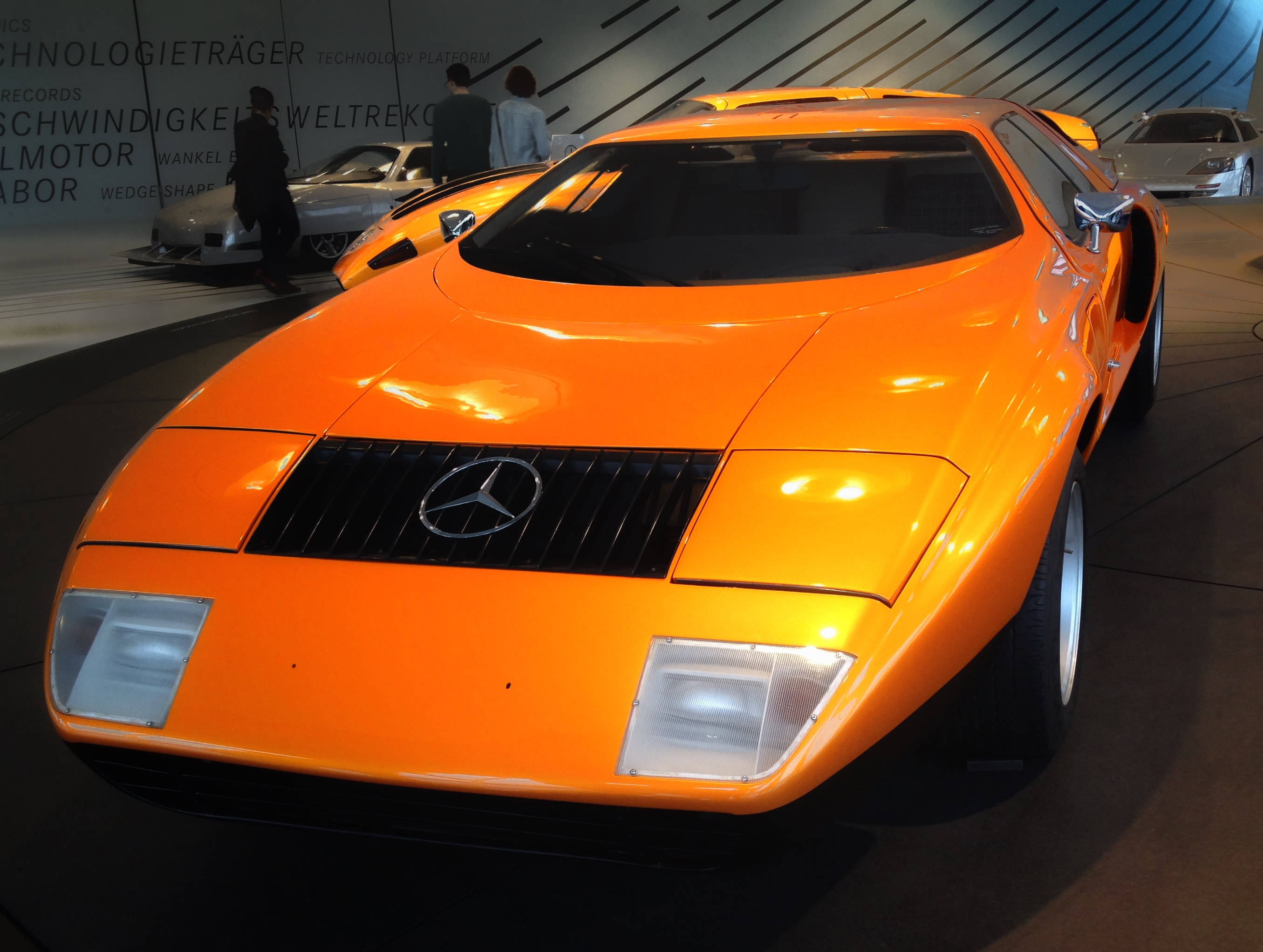 跑車 桌布 壁紙 — 一輛充滿活力的橙色 Mercedes-Benz 跑車在博物館燈光下閃閃發光，擁有流線型空氣動力學設計和大膽的棱角線條。