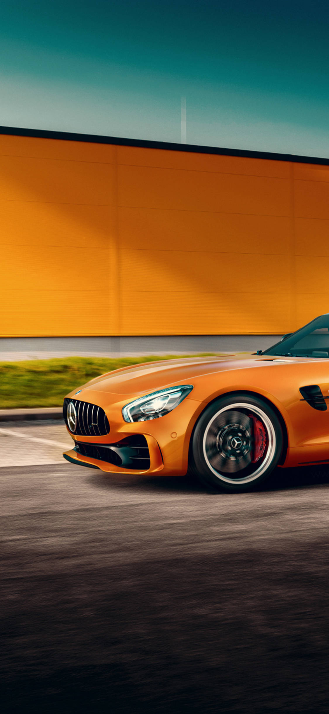X 桌布 壁紙 — 一輛充滿活力的橙色 Mercedes-AMG GT 跑車在晴朗的藍天下飛馳而過一道大膽的橙色牆壁。