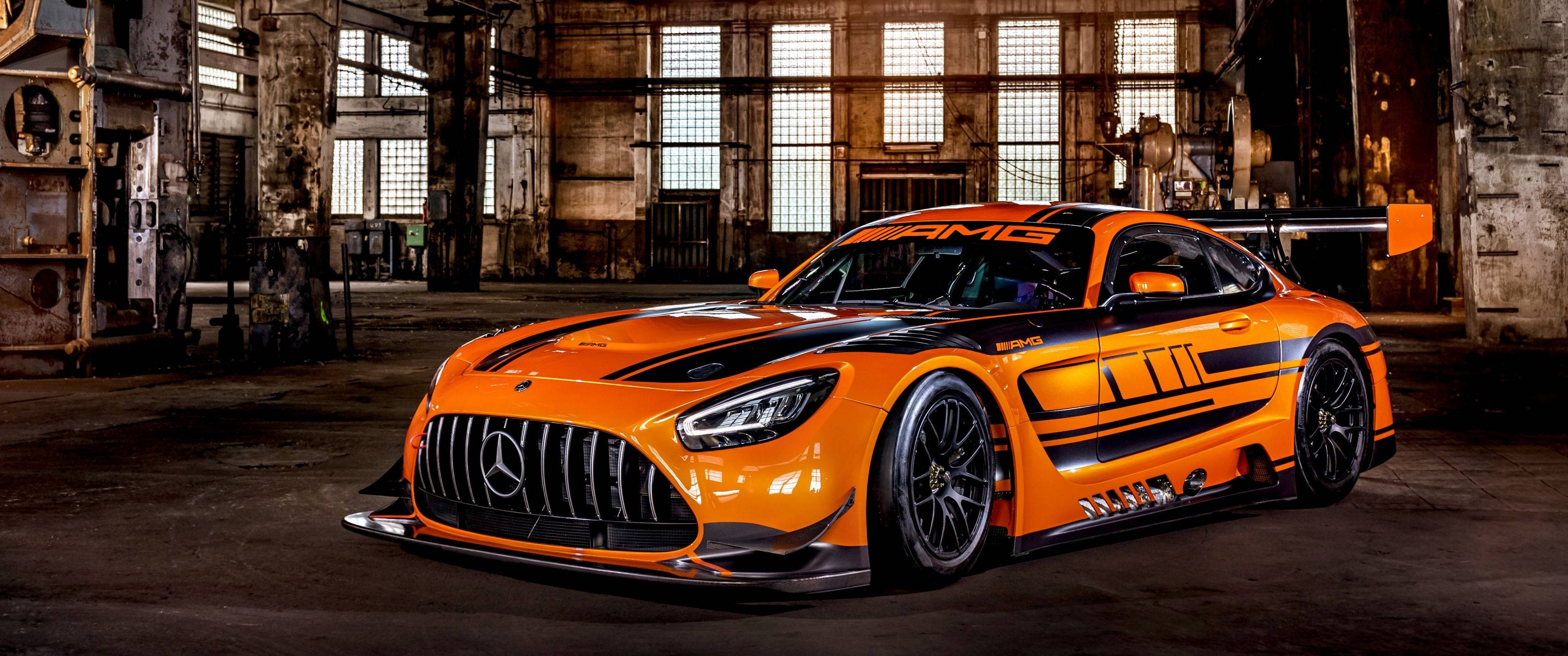 Mercedes 桌布 壁紙 — 一輛充滿活力的橙色 Mercedes-AMG GT3 賽車，帶有黑色點綴，停放在一個風化的工業倉庫中，倉庫有高窗。