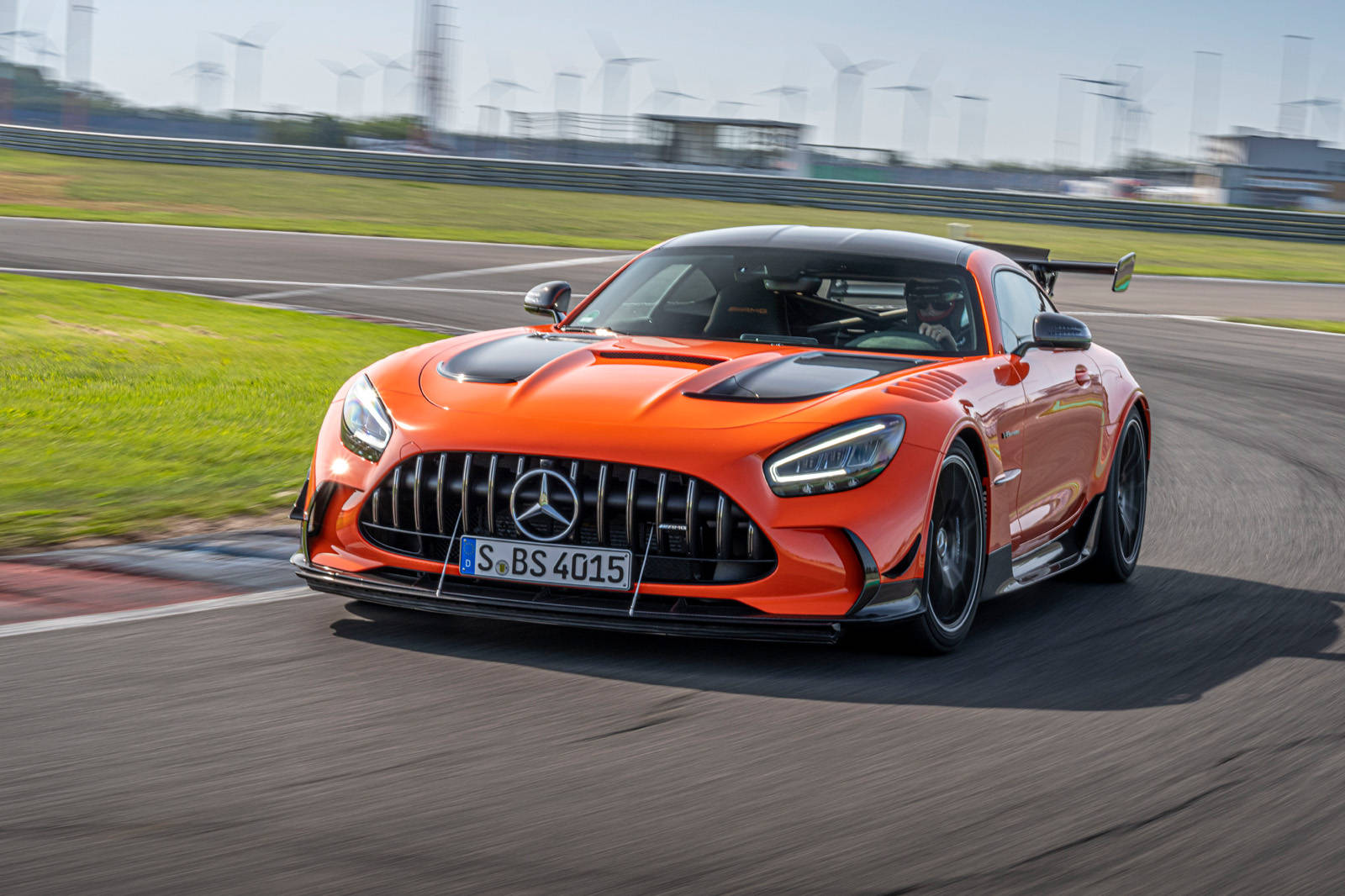 跑車 桌布 壁紙 — 一輛充滿活力的橙色 Mercedes-AMG GT R 賽車在賽道上疾馳，背景模糊中可見風力發電機。