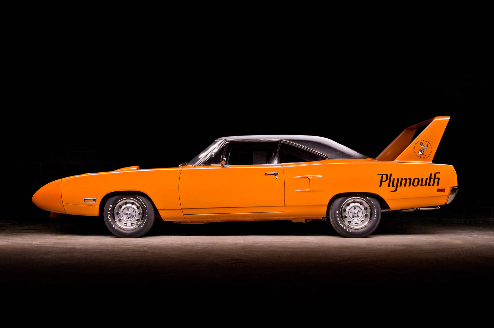 經典汽車 桌布 壁紙 — 一輛充滿活力的橙色1960年代Plymouth Superbird肌肉車，配備黑色車頂和標誌性尾翼，在黑色背景下的戲劇性工作室燈光中展現。
