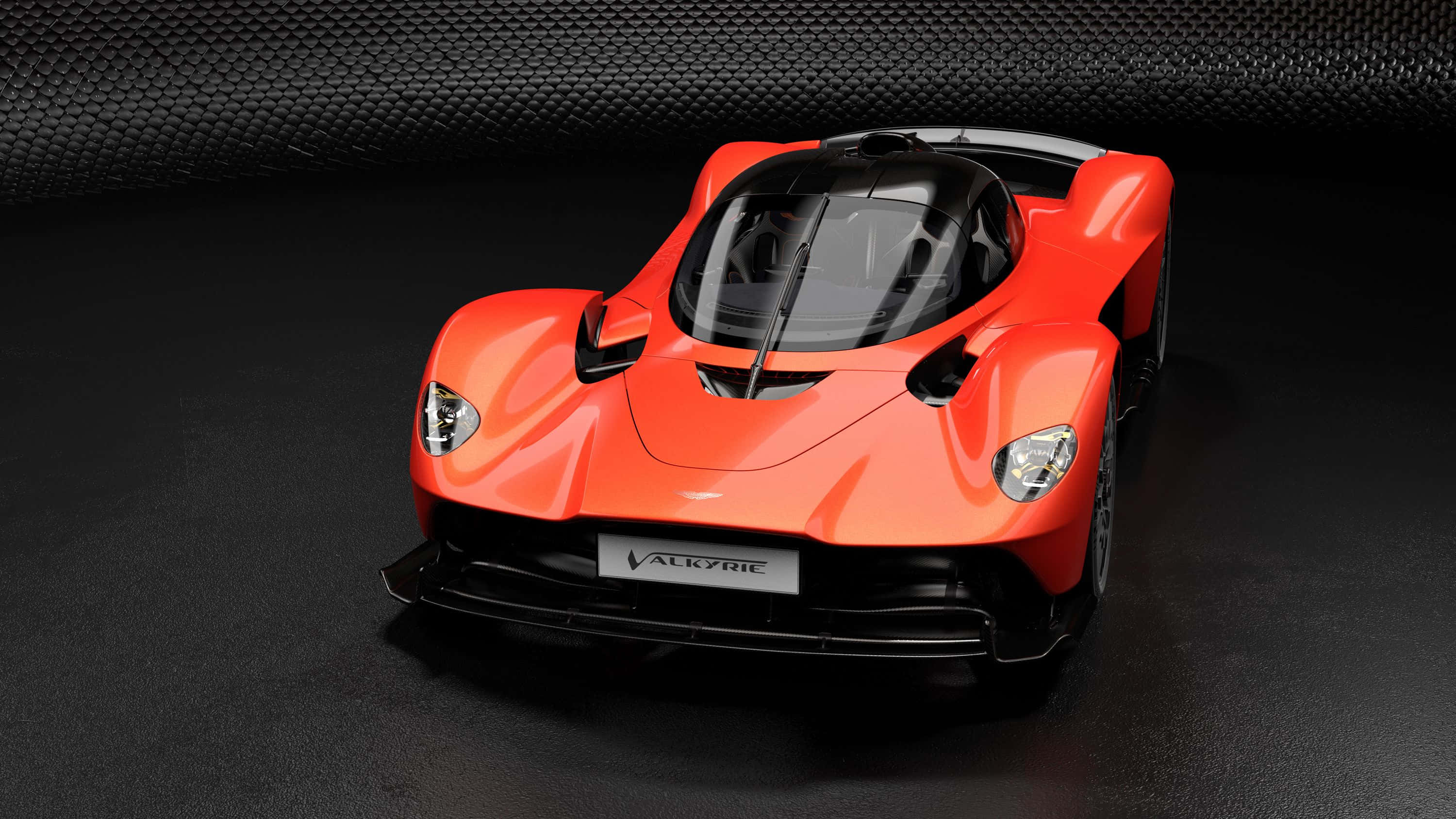 Aston Martin Valkyrie 桌布 壁紙 — 一輛充滿活力的橙色Aston Martin Valkyrie hypercar在工作室燈光下，以深色碳纖維背景襯托下閃閃發光。