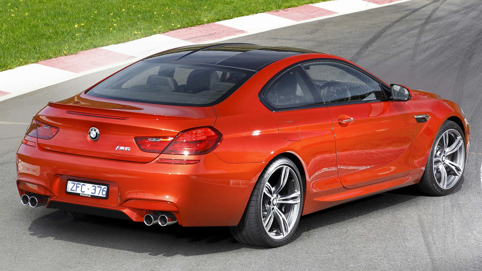 Bmw M6 桌布 壁紙 — 一輛充滿活力的橙色BMW M6雙門跑車在賽道上疾馳，賽道有紅白路緣石，旁邊是綠色草地。