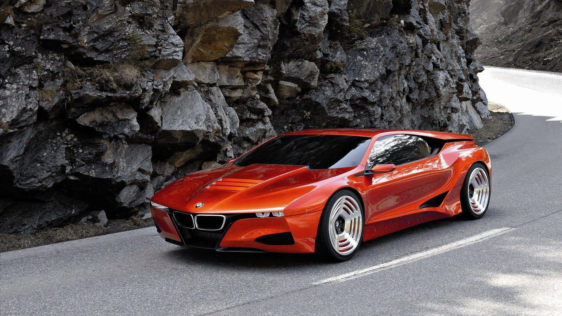 BMW 動圖 桌布 壁紙 — 一輛充滿活力的橙色BMW概念車，採用流線型空氣動力學設計，沿著蜿蜒的山路行駛，旁邊是堅固的灰色岩石 formations。