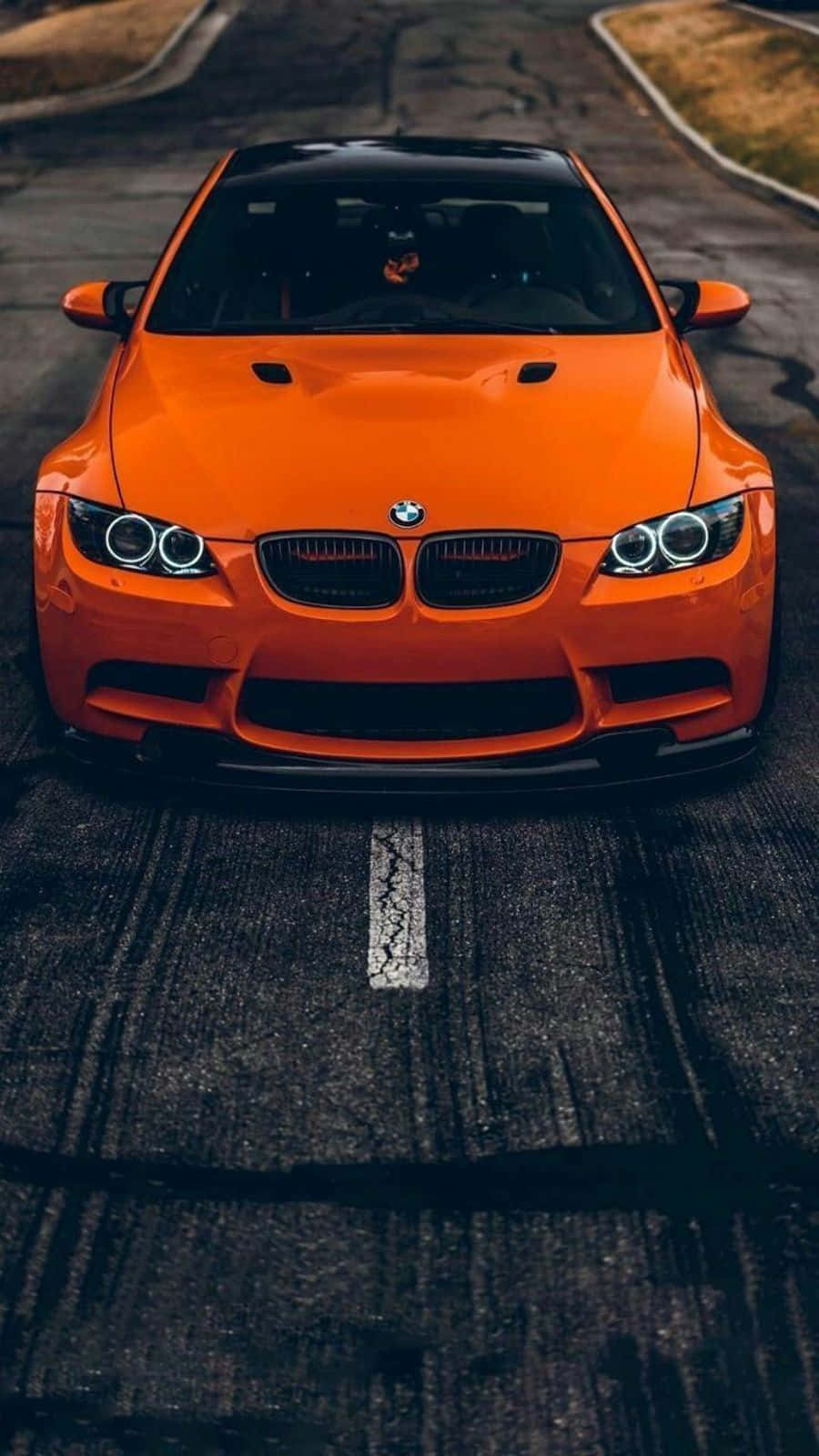 BMW 動圖 桌布 壁紙 — 一輛充滿活力的橙色BMW跑車在帶有裂紋白線的深色瀝青路上向前行駛。