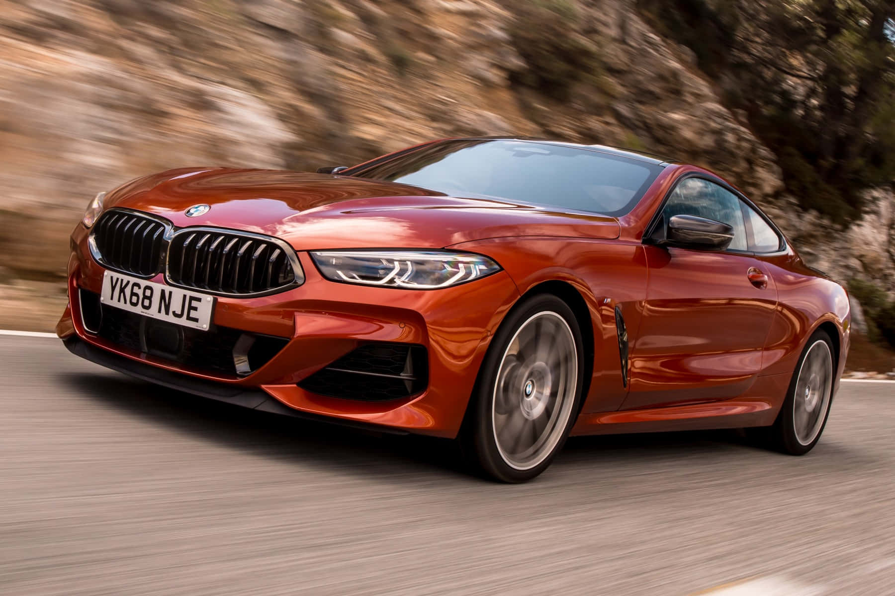 Bmw 8 Series 桌布 壁紙 — 一輛充滿活力的橙色BMW雙門轎跑車沿著蜿蜒的山路疾馳，動態模糊強調了其動感移動。