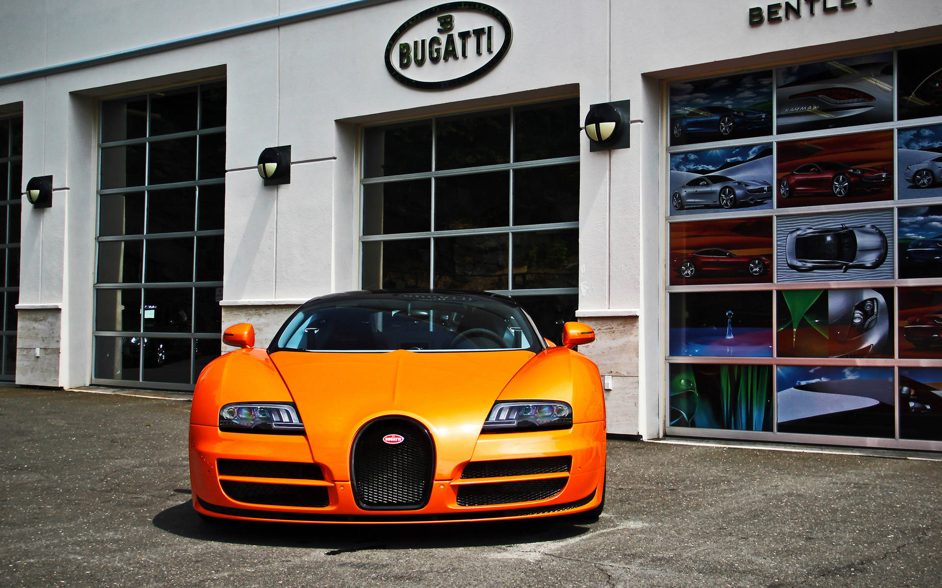 bugatti iPhone 桌布 壁紙 — 一輛充滿活力的橙色Bugatti超級跑車自豪地停在一間豪華經銷商前，玻璃車庫門展示著汽車海報。
