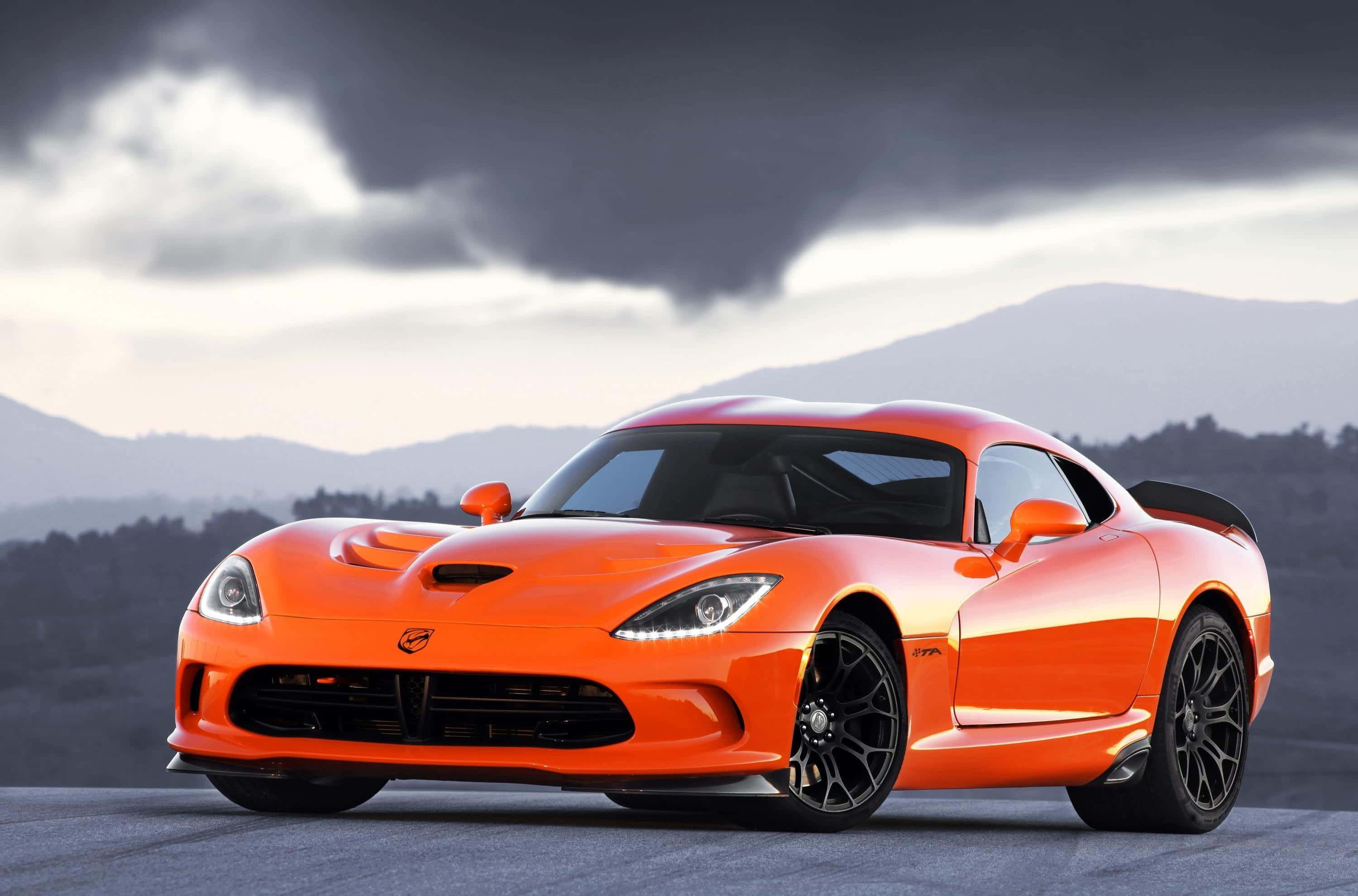 Dodge 桌布 壁紙 — 一輛充滿活力的橙色Dodge Viper跑車在戲劇性的暴風雲下閃閃發光，背景有山脈。