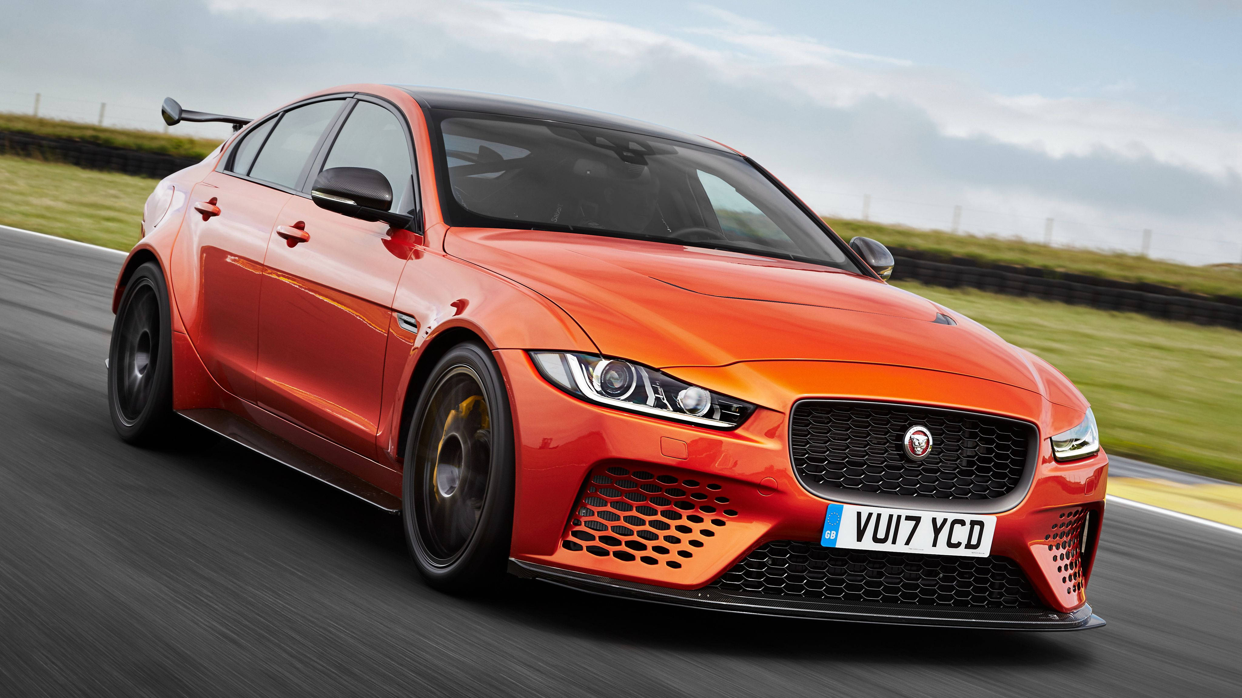 project cars 4K 桌布 壁紙 — 一輛充滿活力的橙色Jaguar XE SV Project 8在賽道上疾馳，背景是模糊的綠色草地和多雲的天空。