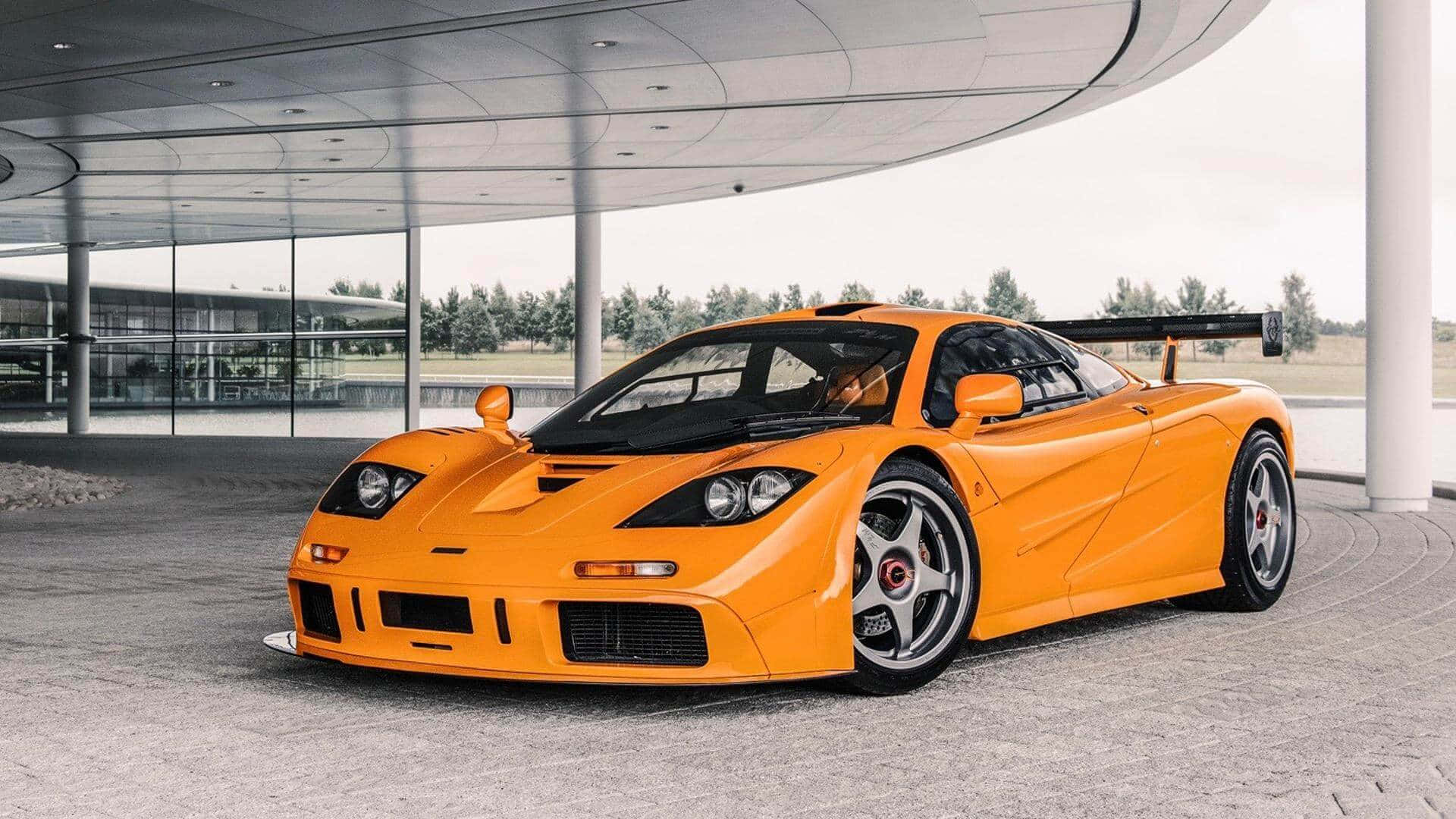 Mclaren F1 桌布 壁紙 — 一輛充滿活力的橙色McLaren F1超級跑車在現代玻璃和鋼製天篷下於日光下閃耀。