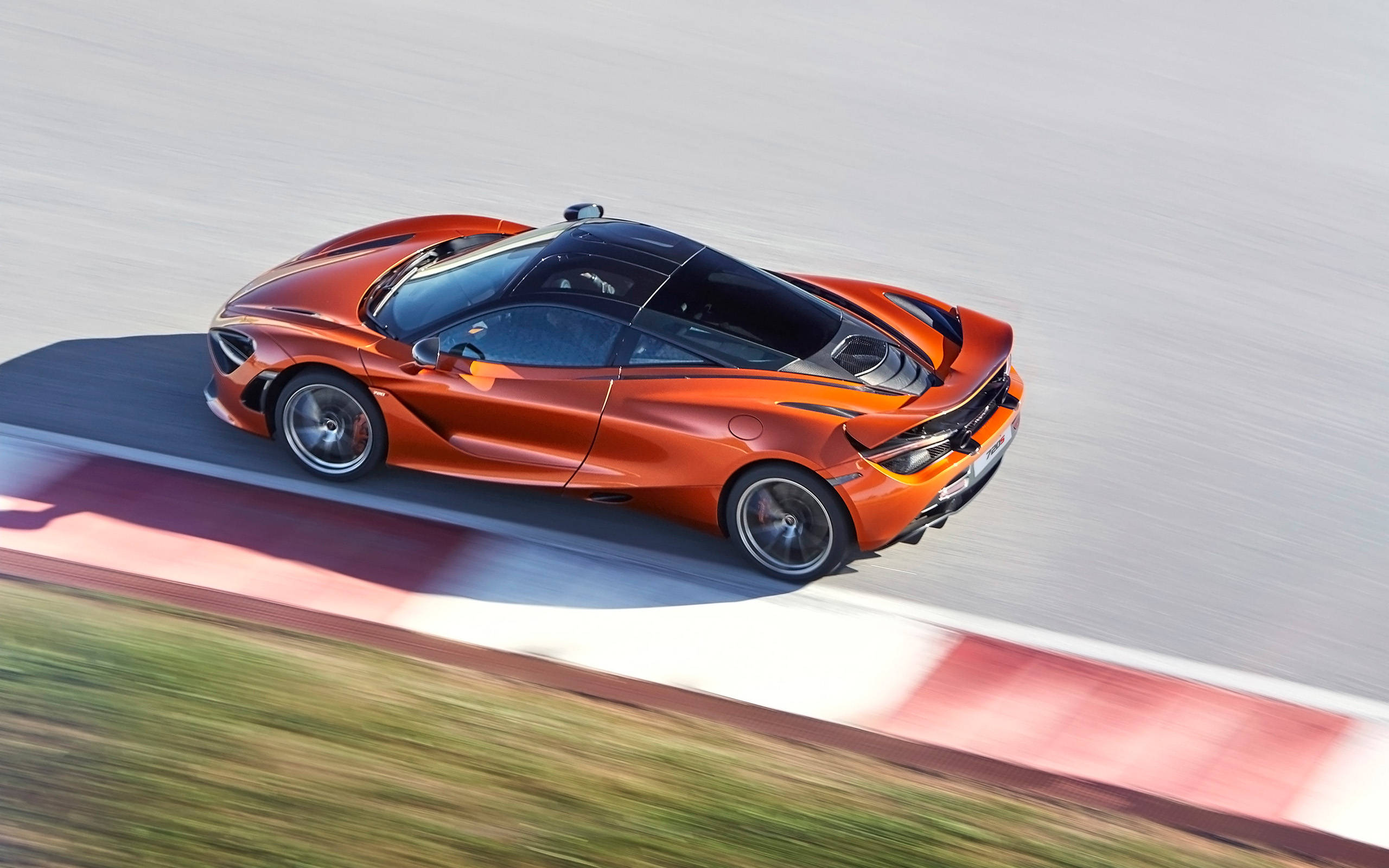 mclaren 720s 4K 桌布 壁紙 — 一輛充滿活力的橙色McLaren跑車在賽道上疾馳，動態模糊強調其高速。