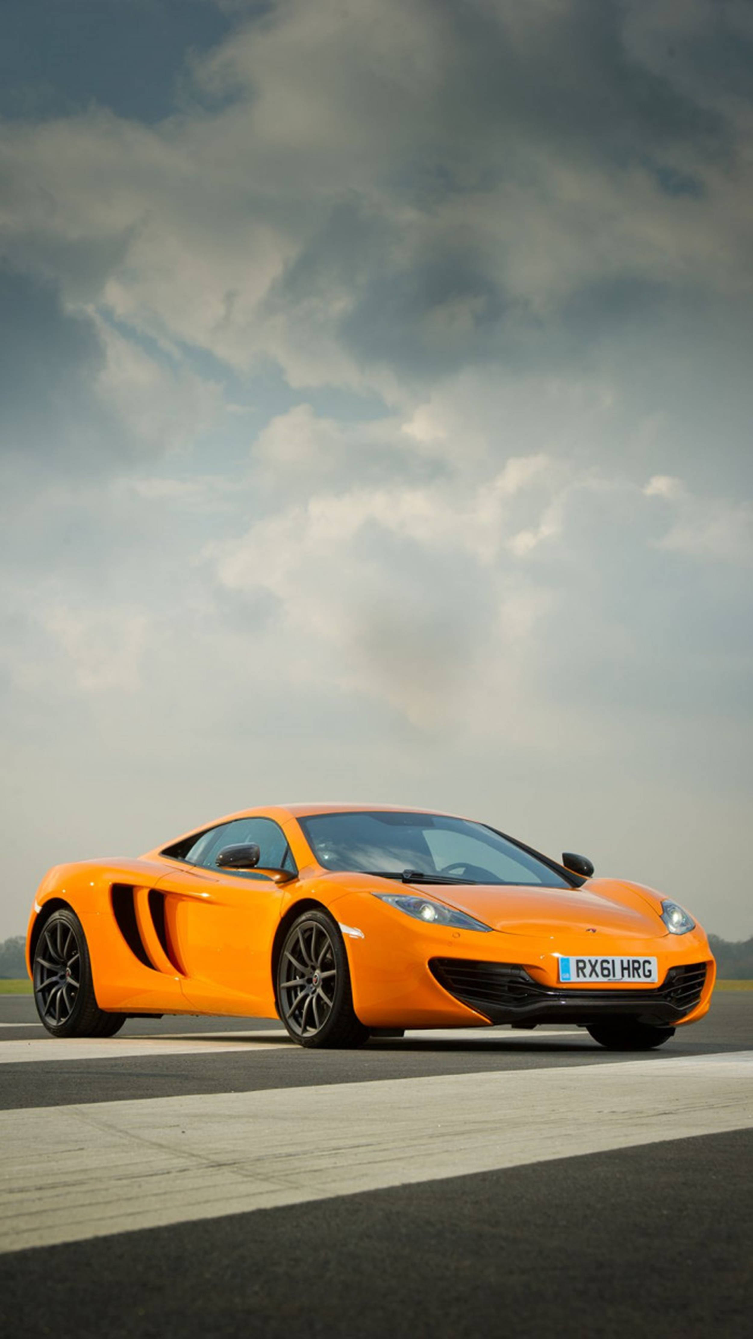 Luxury 桌布 壁紙 — 一輛充滿活力的橙色McLaren跑車停在賽道上，天空烏雲密布，氣氛戲劇化。