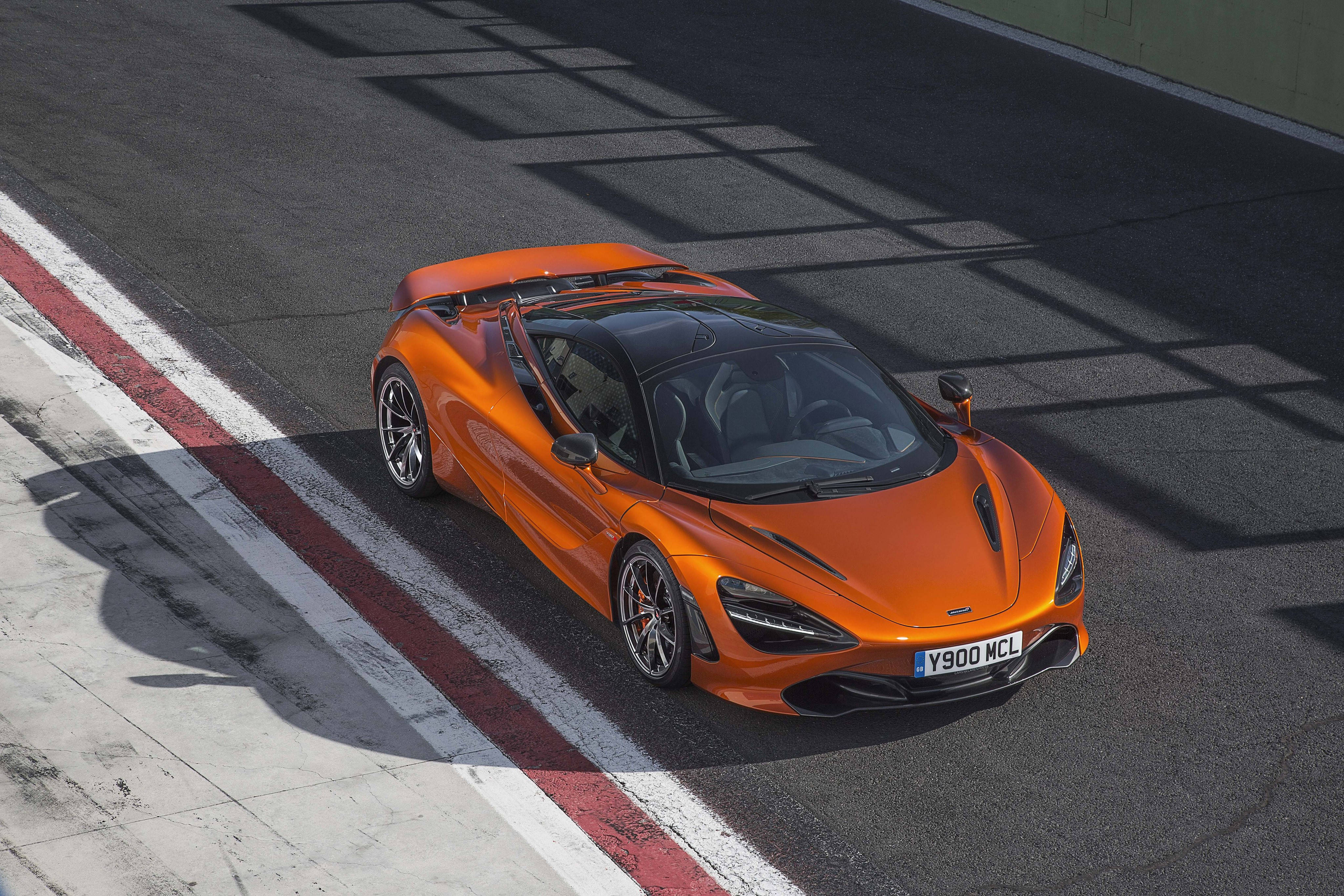 mclaren 720s 4K 桌布 壁紙 — 一輛充滿活力的橙色McLaren 720S跑車在陽光照耀的賽道上奔馳，上方結構投下清晰的陰影。