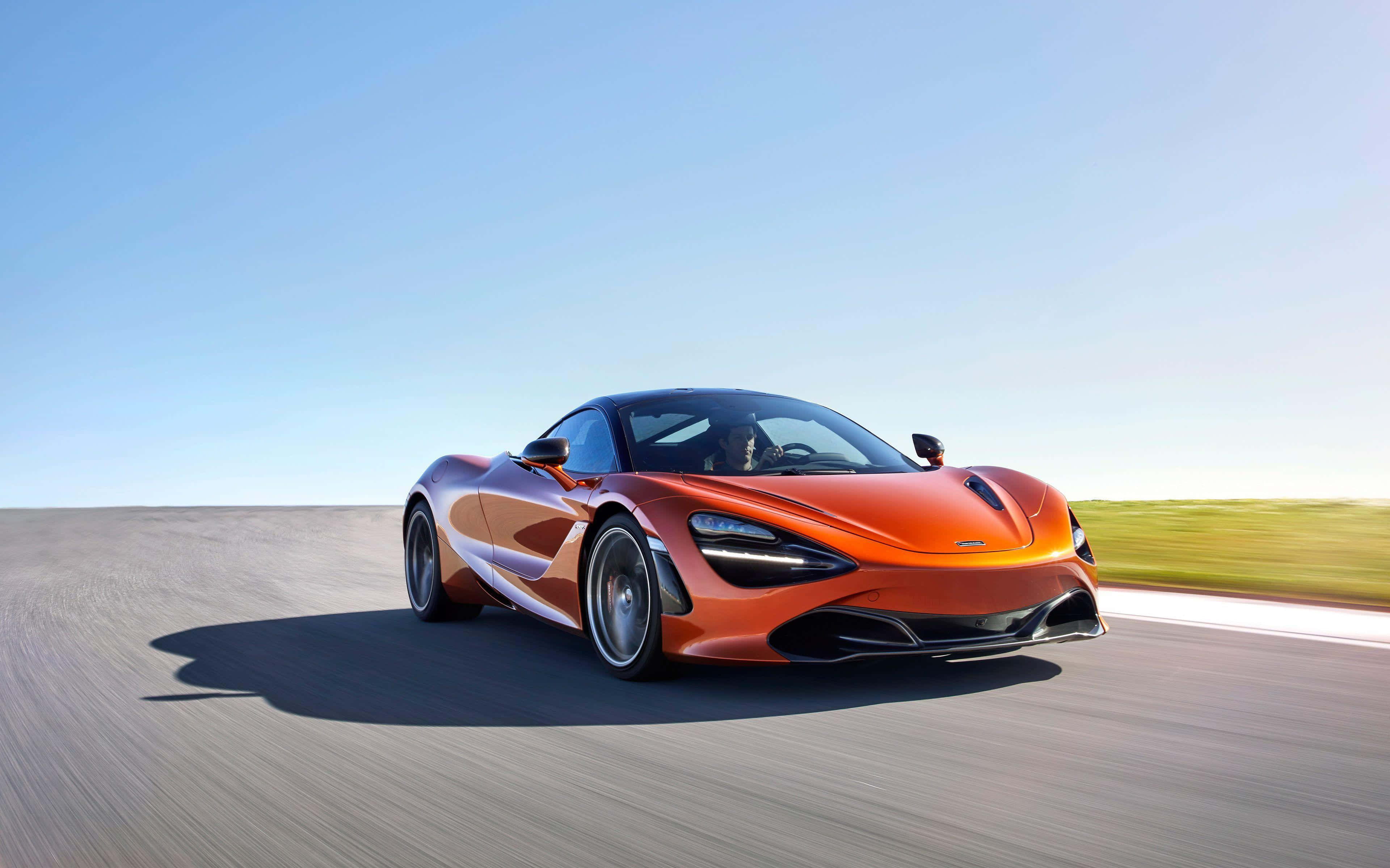 麥拉倫 720S 桌布 壁紙 — 一輛充滿活力的橙色McLaren跑車在陽光明媚的沙漠公路上疾馳，帶有模糊的動感和清澈的藍天。