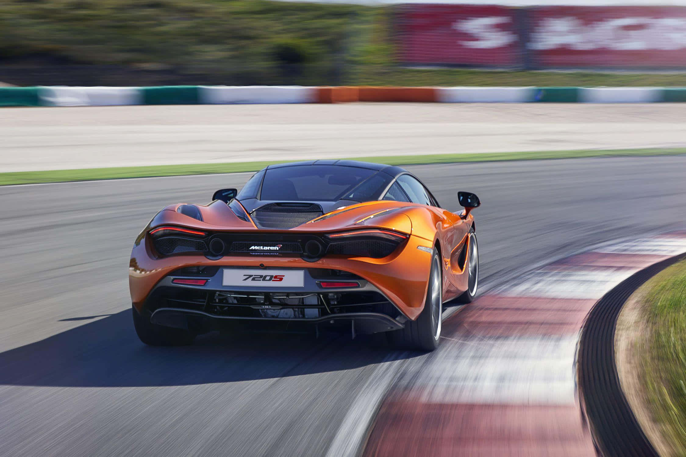 Mclaren 720s 桌布 壁紙 — 一輛充滿活力的橙色McLaren 720S在賽道彎道上高速行駛，動態模糊強調其高速。