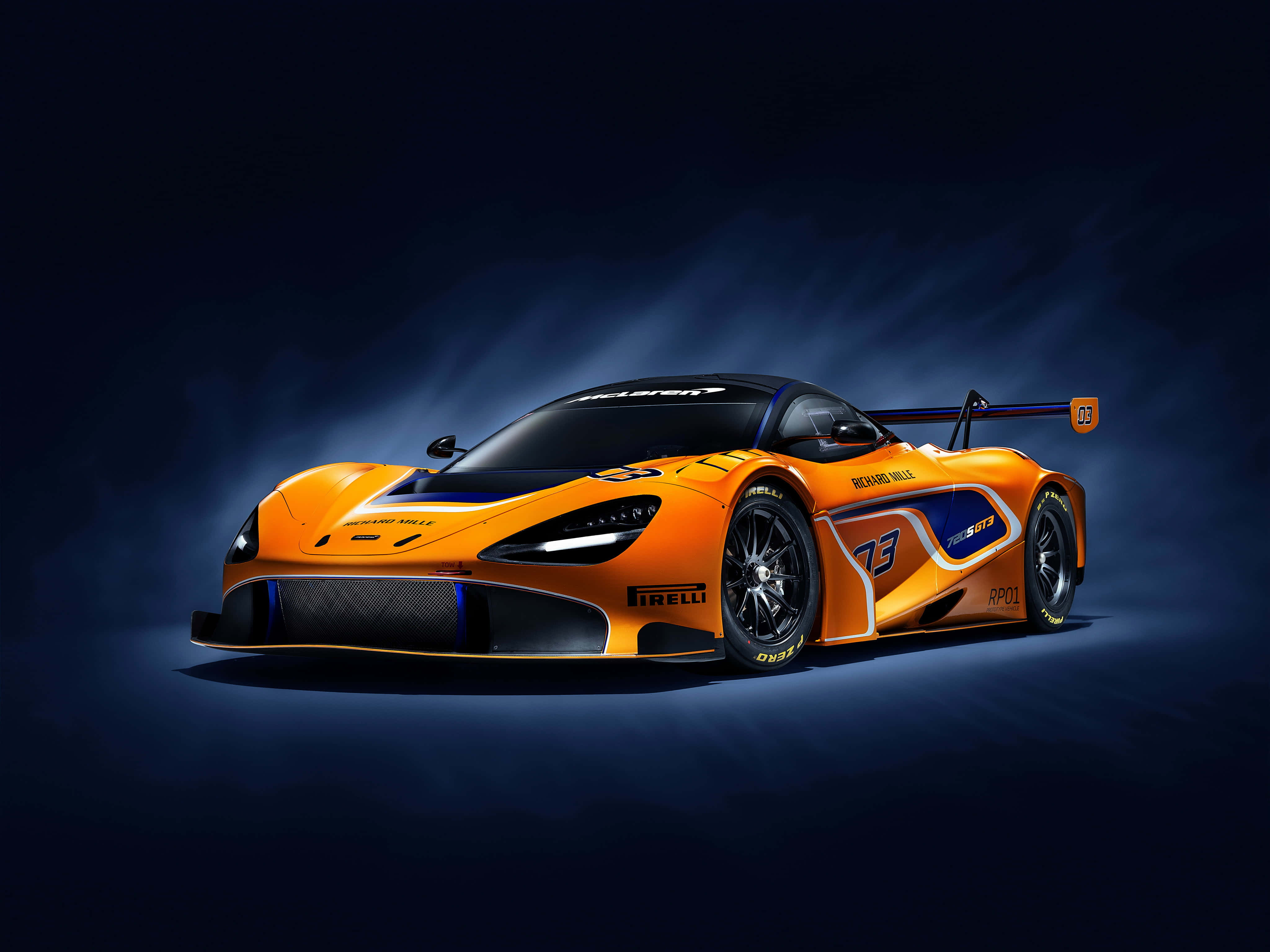 Mclaren 720s 桌布 壁紙 — 一輛充滿活力的橙色McLaren SRT賽車，帶有藍色點綴和73號，在深藍色背景下的戲劇性工作室燈光中閃耀。