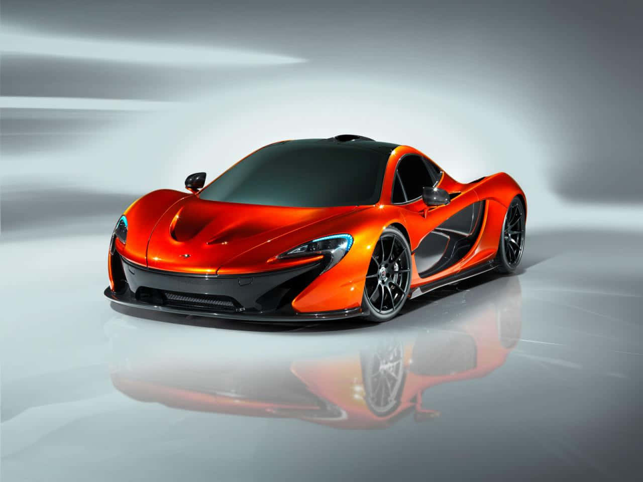 麥拉倫 桌布 壁紙 — 一輛充滿活力的橙色McLaren P1超級跑車在工作室燈光下閃閃發光，並在拋光地板上完美反射。