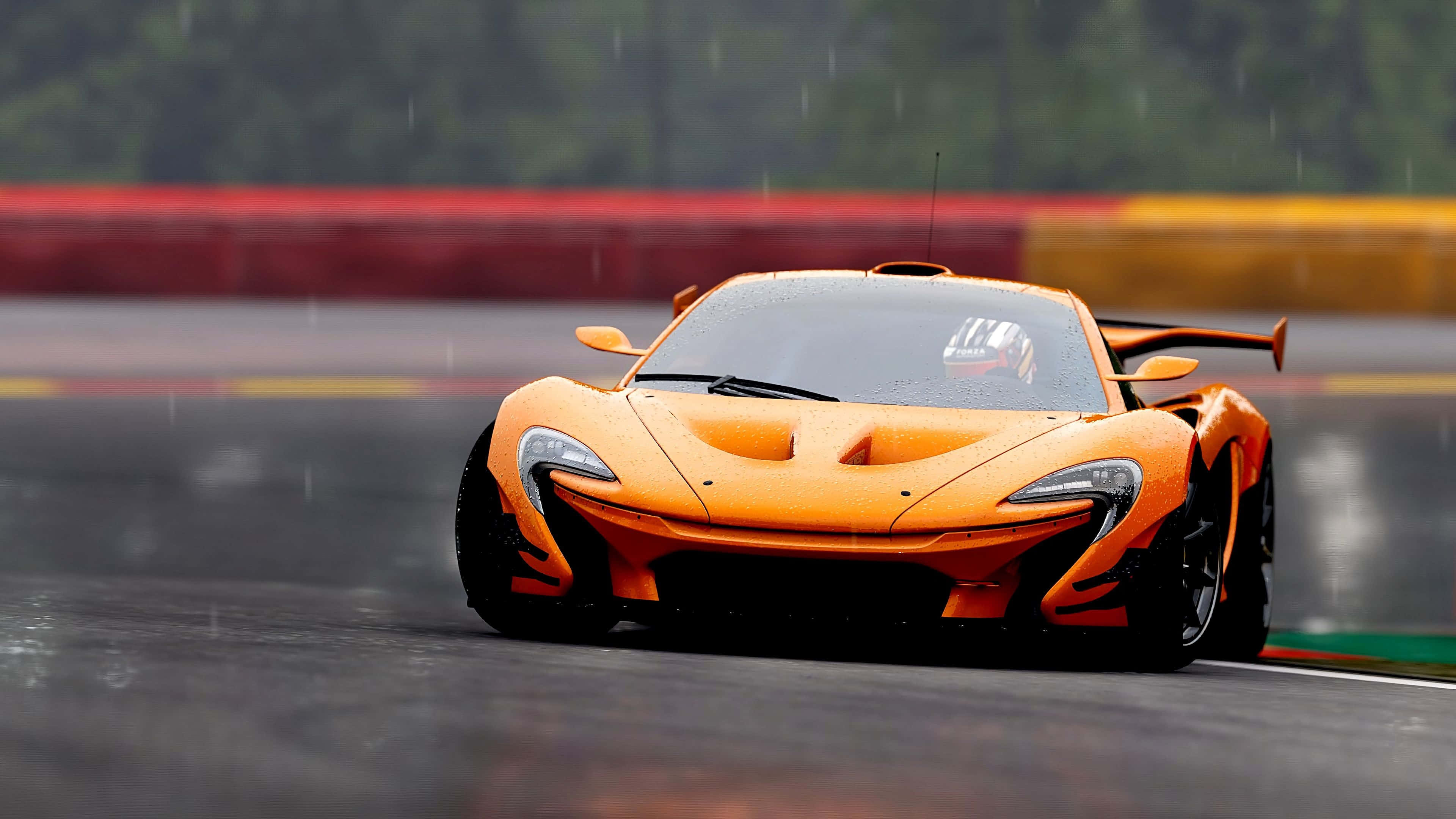 麥拉倫 桌布 壁紙 — 一輛充滿活力的橙色McLaren P1在潮濕的賽道上奔馳，雨滴在其流線型的空氣動力學車身上閃閃發光。