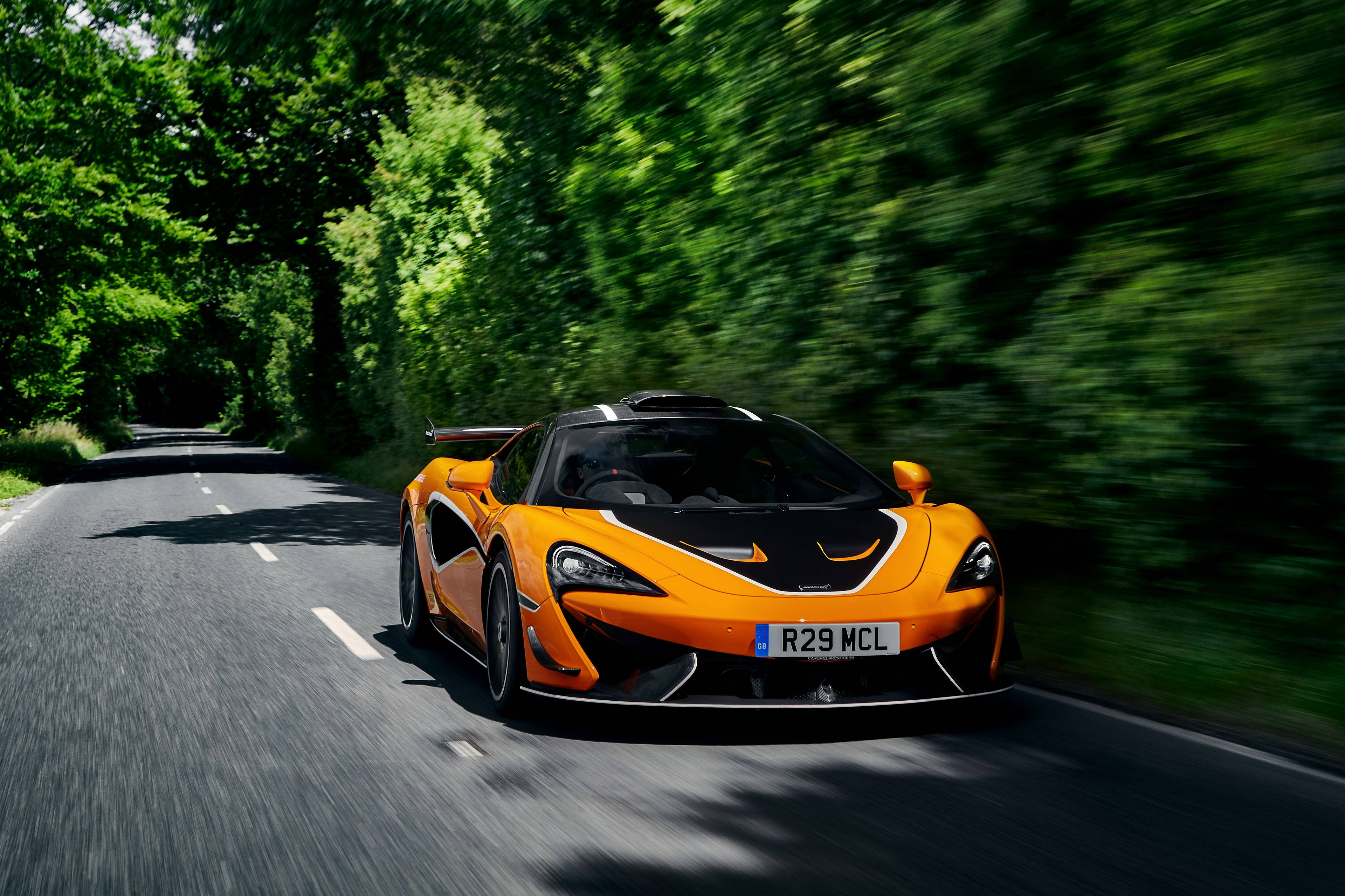 Auto Racing 桌布 壁紙 — 一輛充滿活力的橙色McLaren跑車在樹木成蔭的道路上飛馳，動態模糊效果強調了其速度。