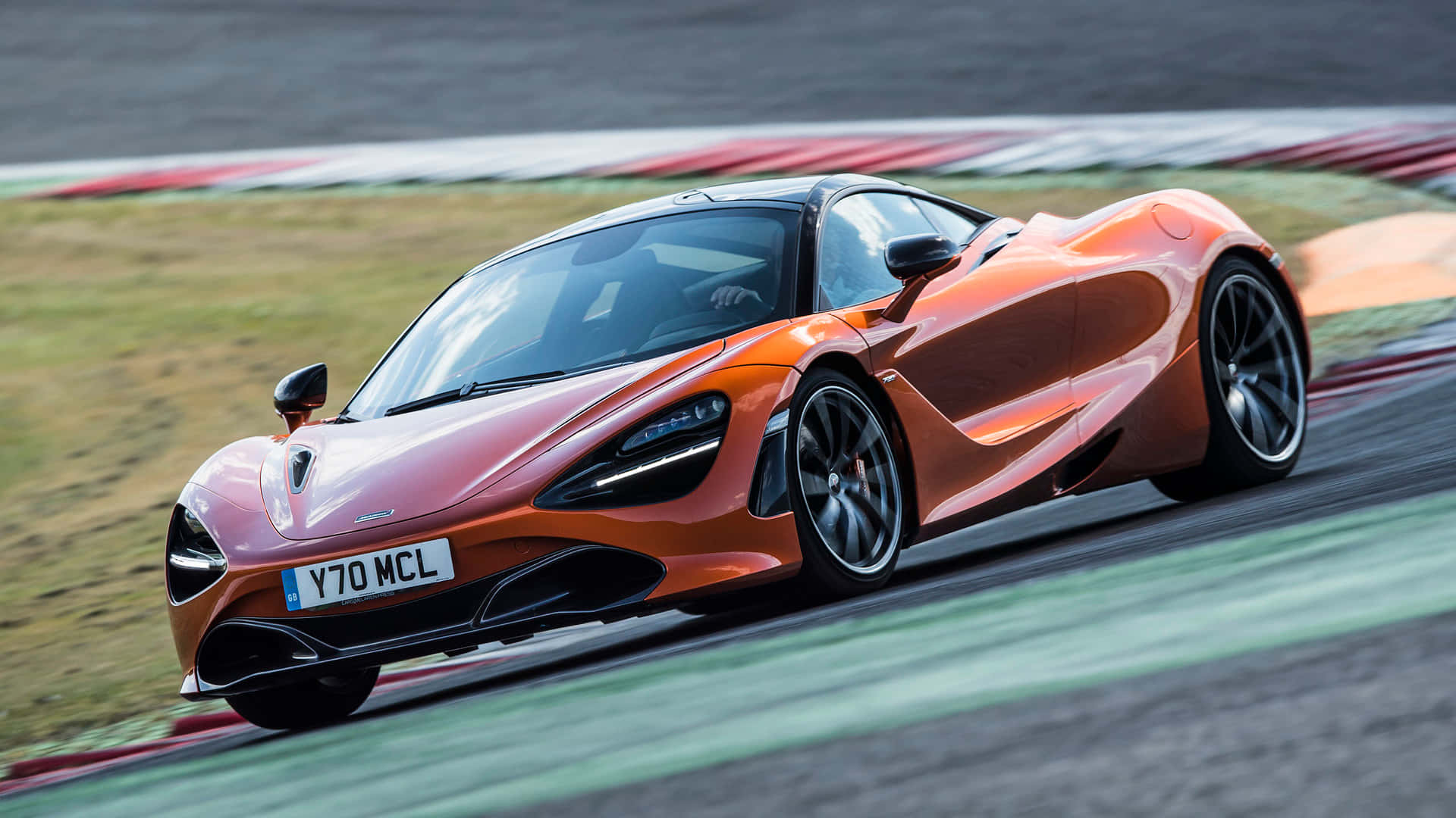 Race Track 桌布 壁紙 — 一輛充滿活力的橙色McLaren 720S在賽道上疾馳，帶有動態模糊效果和紅白路緣。