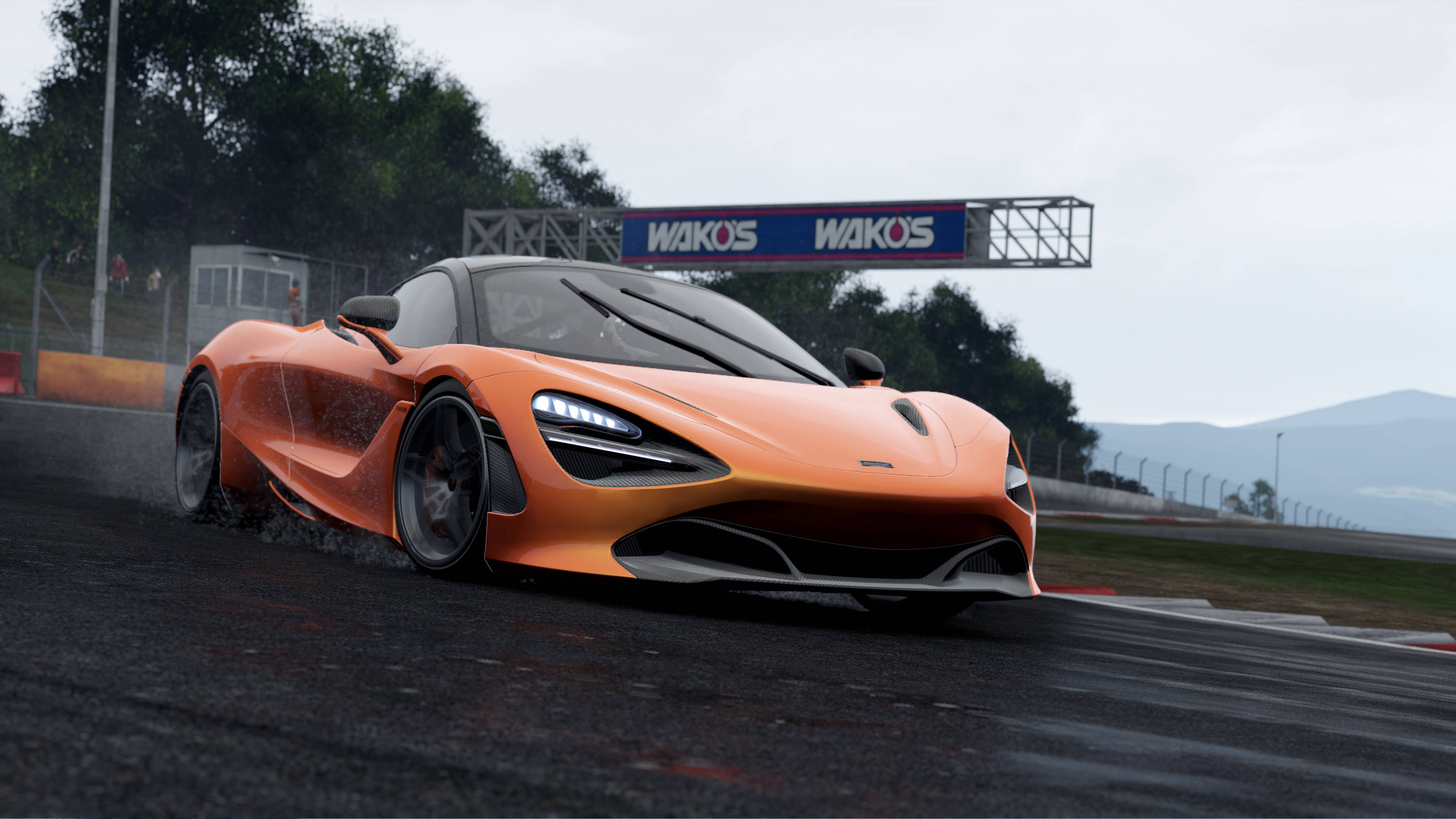 cars 桌布 壁紙 — 一輛充滿活力的橙色McLaren跑車在潮濕的賽道上飄移，天空多雲，遠處有山丘，頭頂有WAKOS標誌。