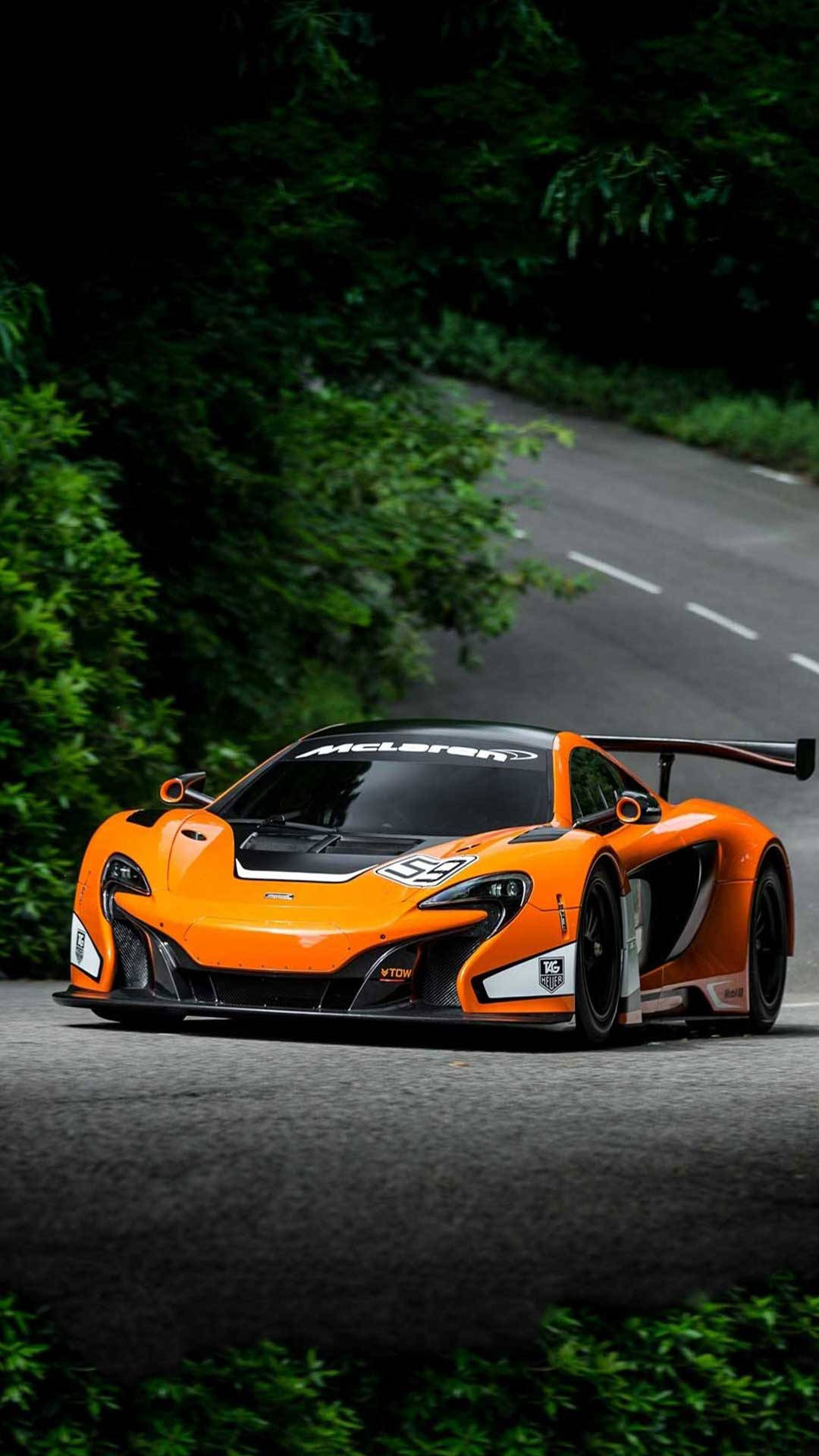 汽車 iPhone 壁紙 桌布 壁紙 — 一輛充滿活力的橙色McLaren賽車在蜿蜒的森林道路上疾馳，周圍環繞著茂密的綠色樹葉。