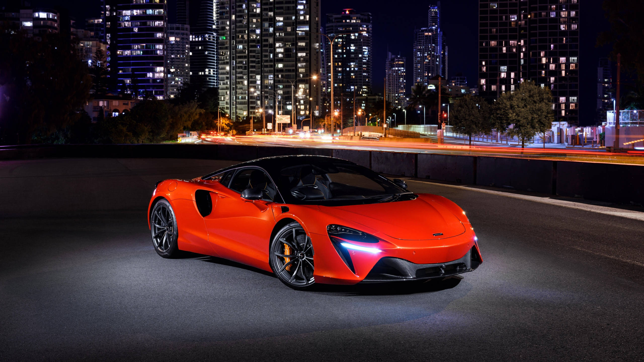 跑車 桌布 壁紙 — 一輛充滿活力的橙色McLaren跑車在夜間城市道路上，在街燈下閃耀，背後有模糊的車流痕跡。