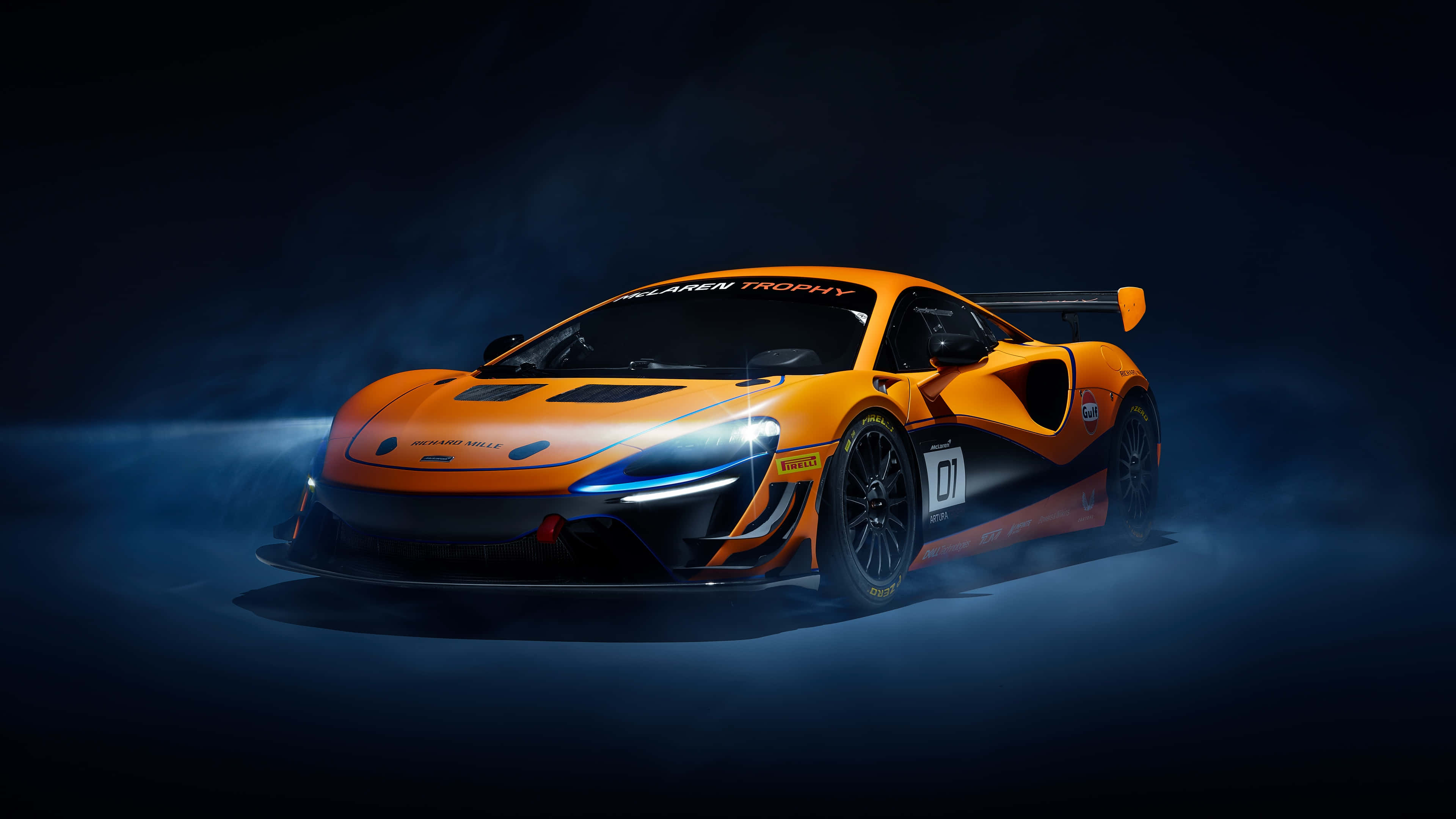cars 桌布 壁紙 — 一輛充滿活力的橙色McLaren賽車在戲劇性的燈光下閃耀，藍色煙霧在其激進的空氣動力學設計周圍旋轉。