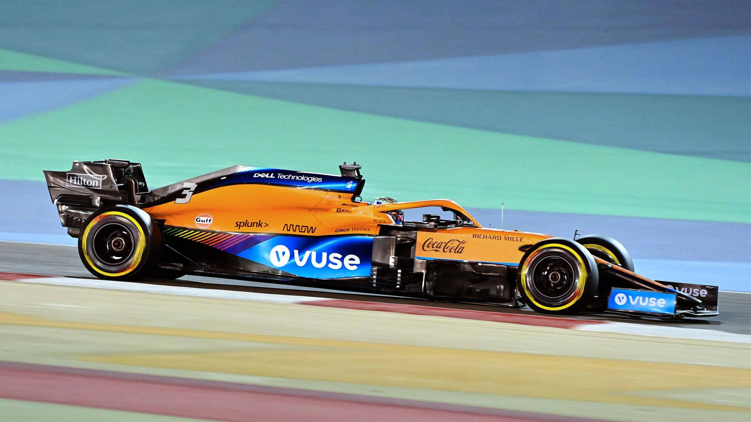 運動 桌布 壁紙 — 一輛充滿活力的橙色McLaren一級方程式賽車在賽道上疾馳，帶有動態模糊和色彩繽紛的贊助商標誌。