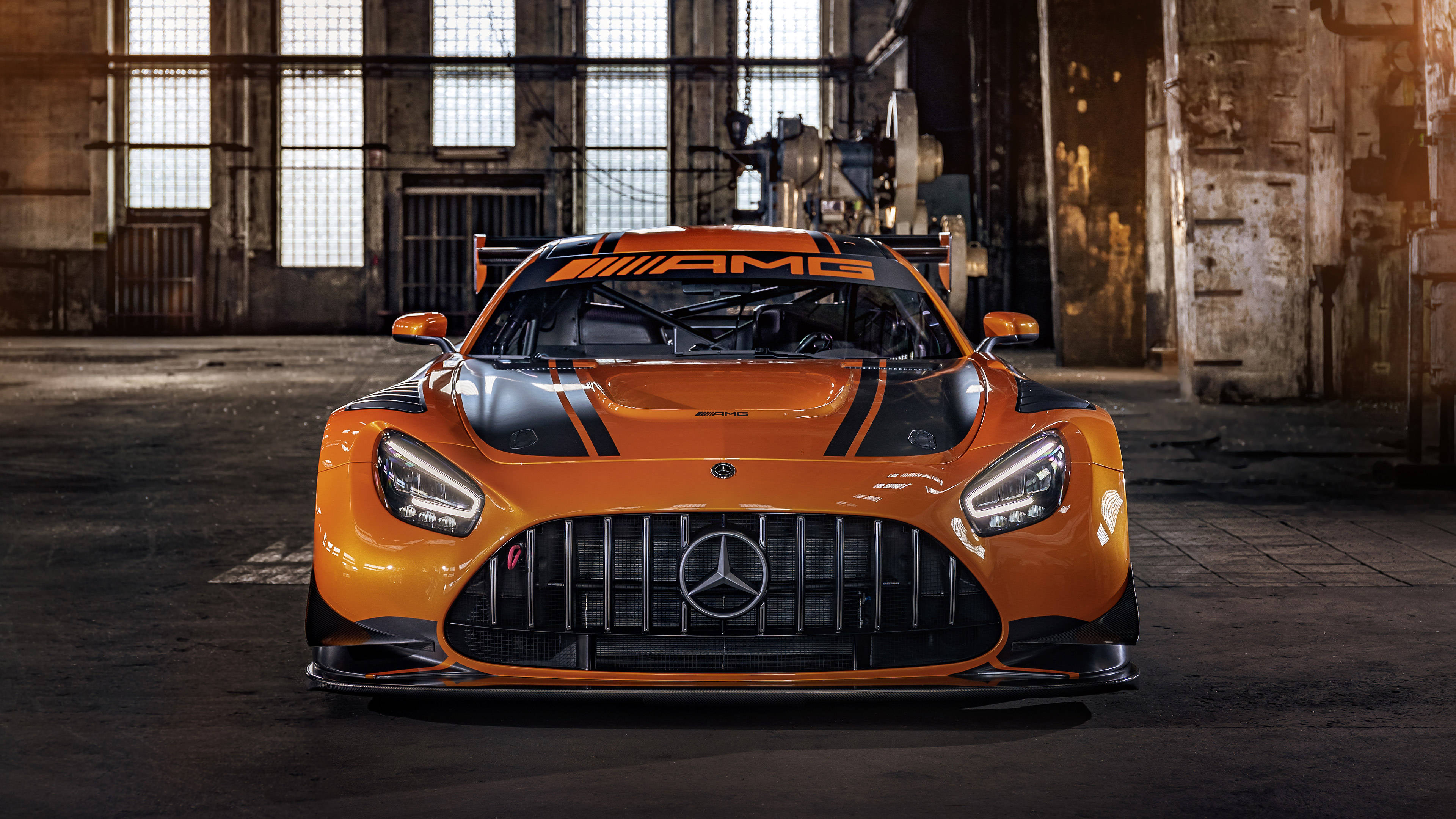 R 桌布 壁紙 — 一輛充滿活力的橙色Mercedes-AMG GT3賽車在一個有高窗和混凝土地板的骯髒工業倉庫中面向前方。