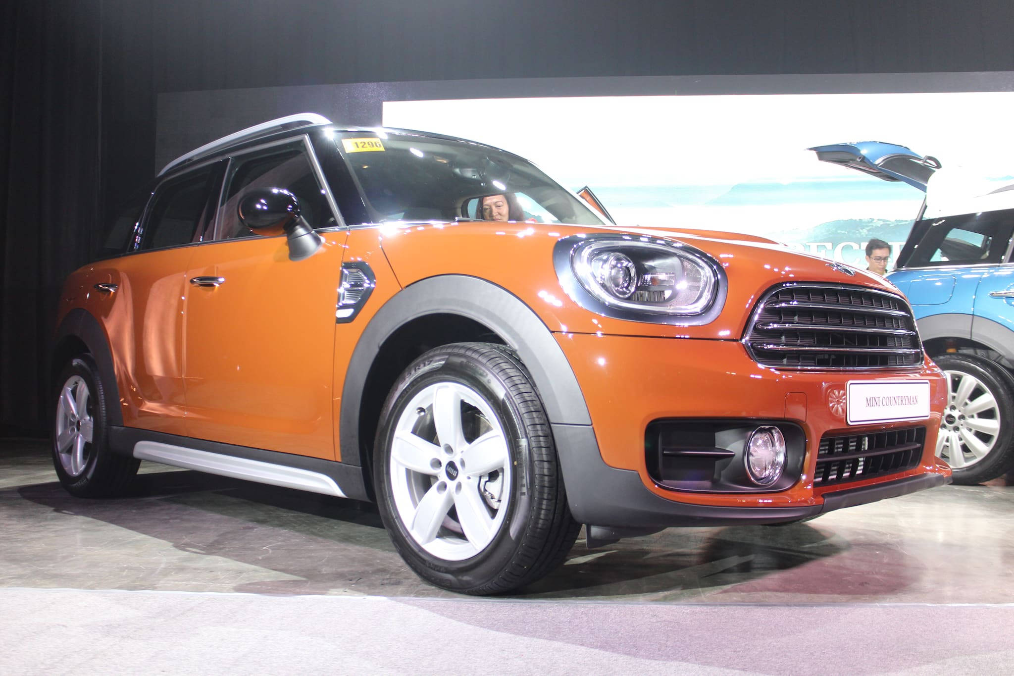 Mini 桌布 壁紙 — 一輛充滿活力的橙色MINI Countryman SUV在車展的明亮燈光下閃閃發光，車內可見一人。