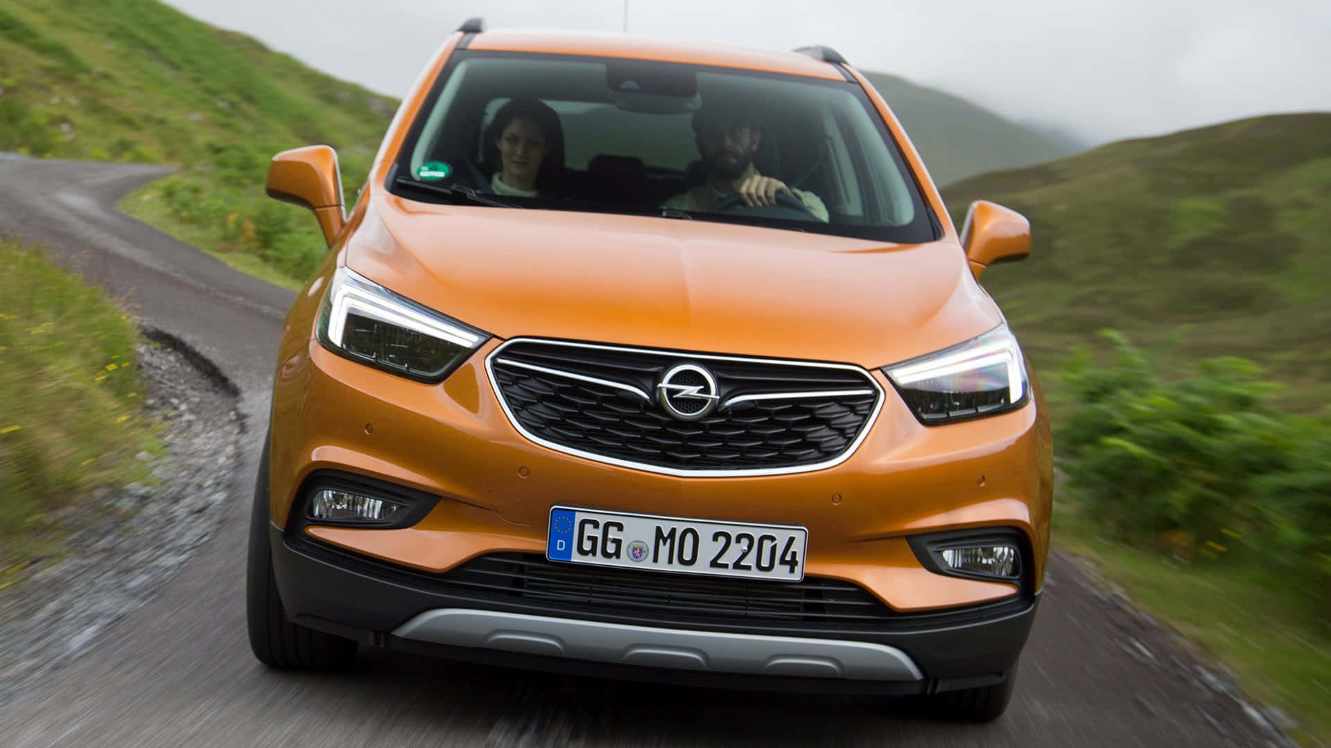 Opel Mokka 桌布 壁紙 — 一輛充滿活力的橙色Opel SUV沿著蜿蜒的山路行駛，車內有兩個人。