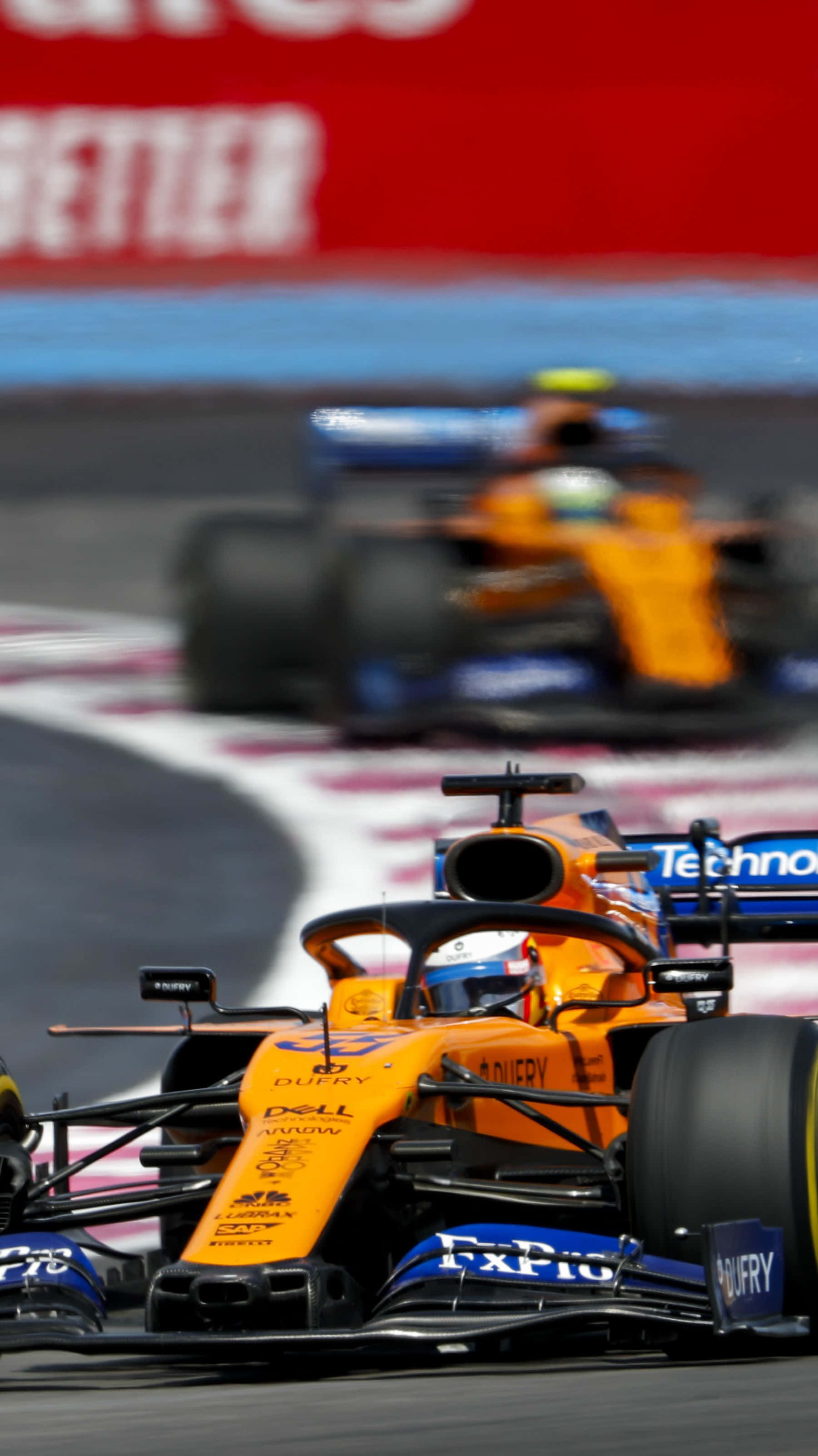 F1 2016 桌布 壁紙 — 一輛充滿活力的橙色一級方程式賽車在賽道彎角急轉，身後有模糊的競爭對手。