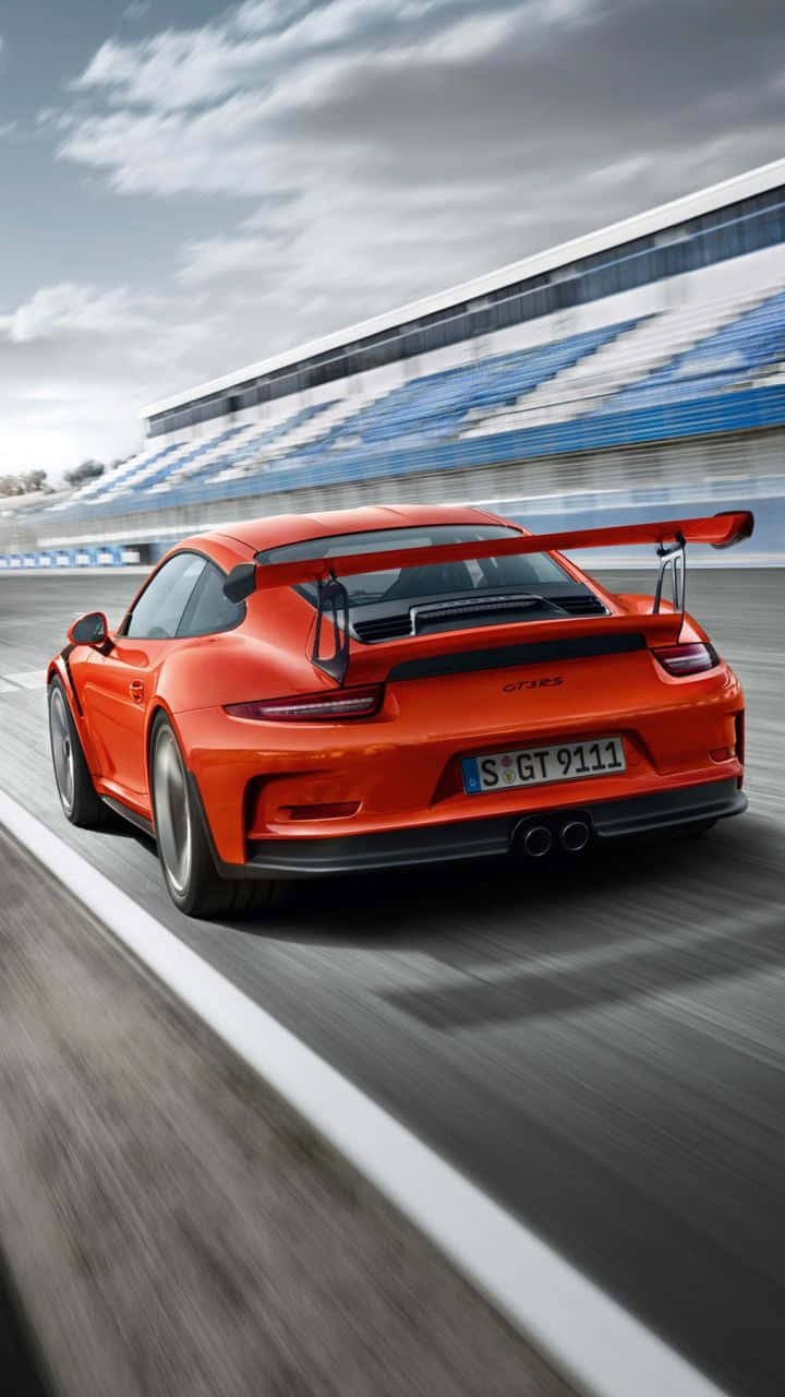911 iPhone 桌布 壁紙 — 一輛充滿活力的橙色保時捷911 GT3 RS在賽道上奔馳，背景是模糊的看台。