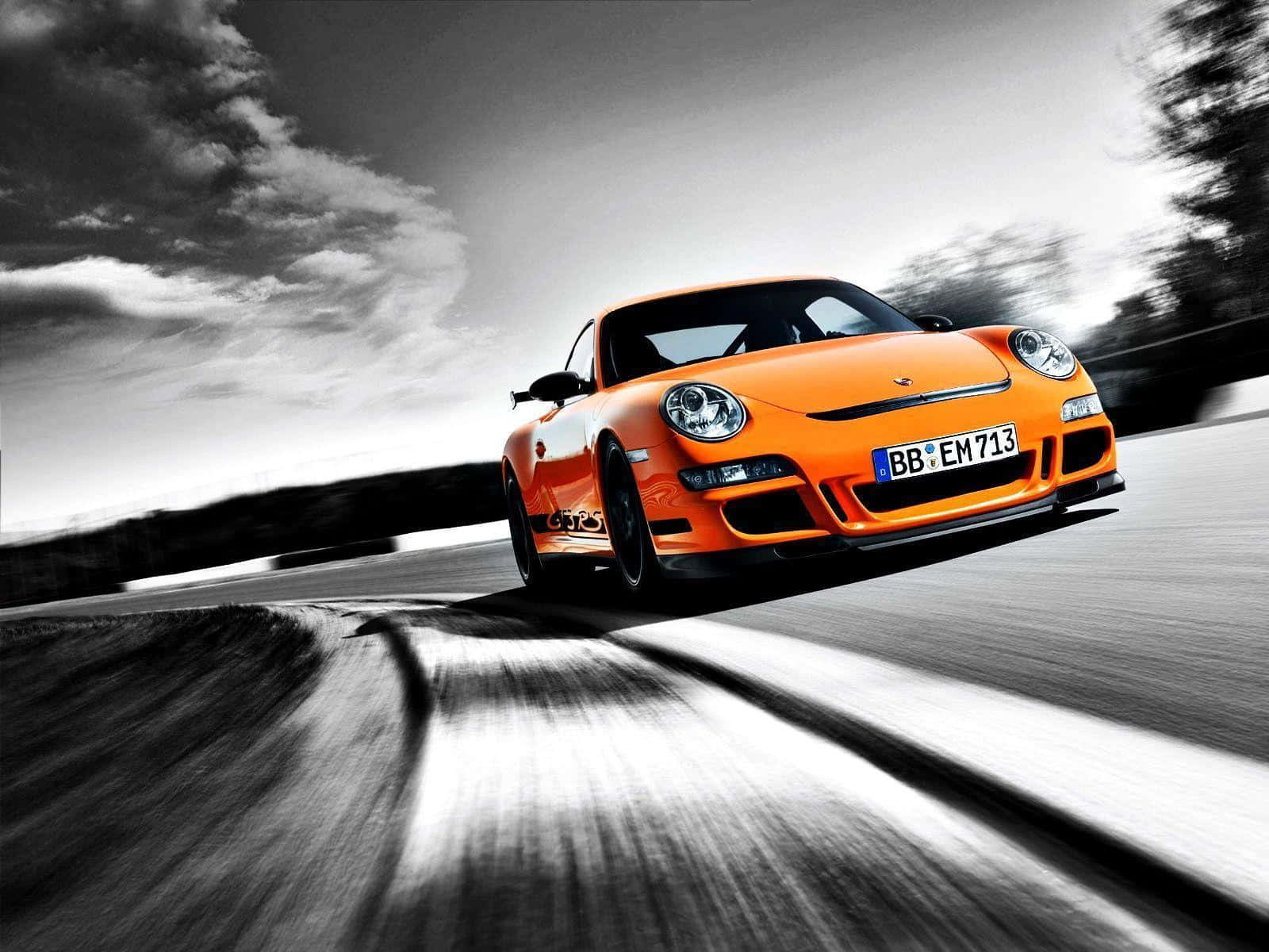 Best Car 桌布 壁紙 — 一輛充滿活力的橙色保時捷911 GT3 RS在戲劇性的單色天空下，沿著模糊的賽道疾馳。