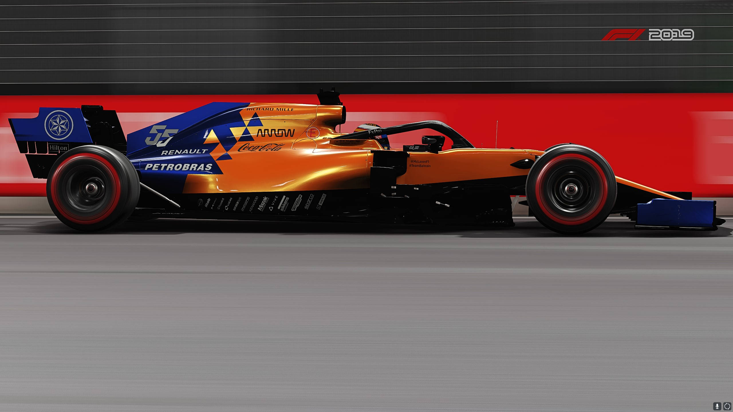 F1 2019 壁紙 桌布 壁紙 — 一輛充滿活力的橙色和藍色一級方程式賽車，帶著動態模糊效果，高速駛過紅色和黑色的賽道護欄。