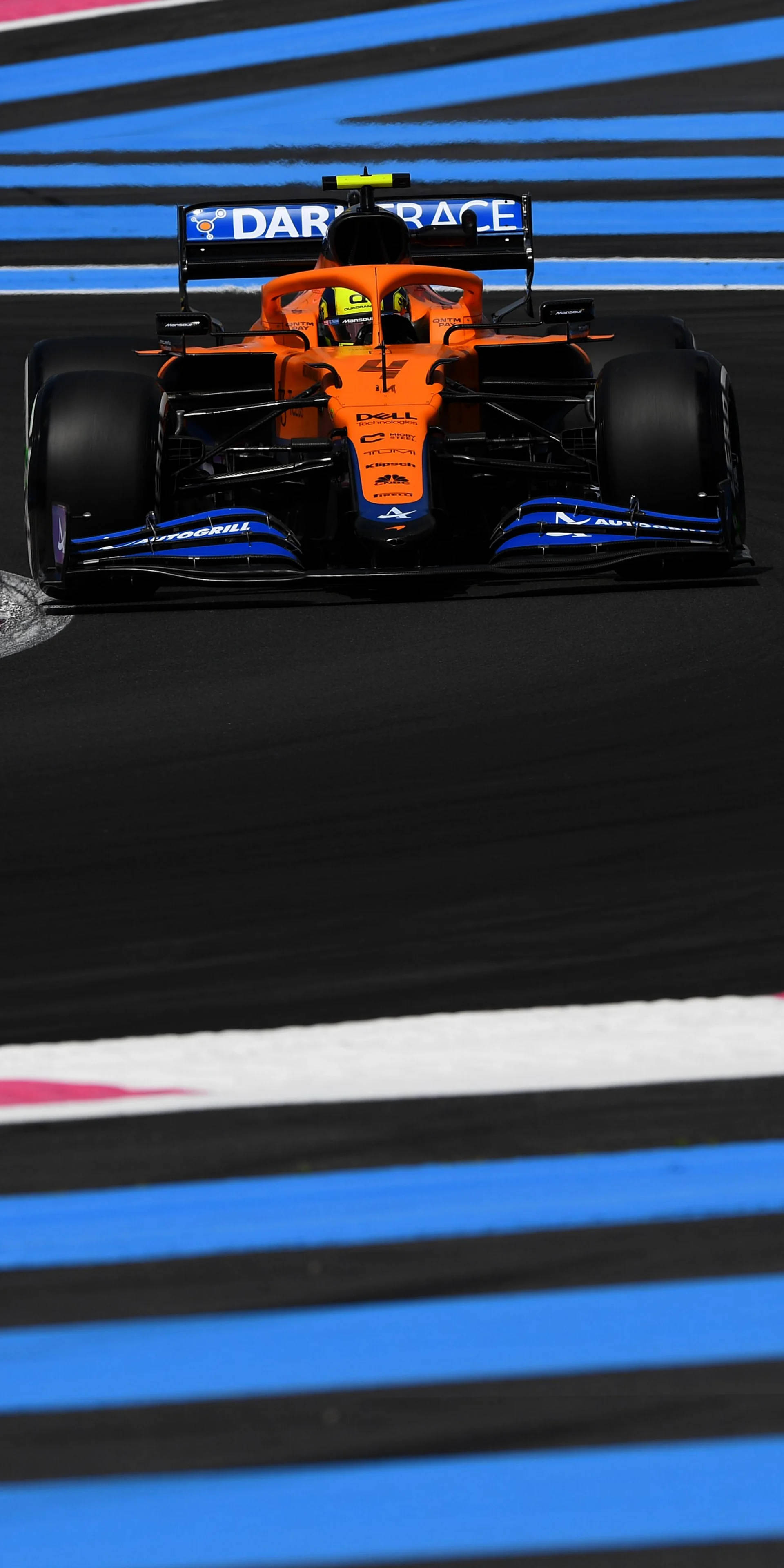 Racing 桌布 壁紙 — 一輛充滿活力的橙色和藍色一級方程式賽車在明亮的日光下沿著賽道飛馳，賽道上有大膽的藍色和白色路緣。