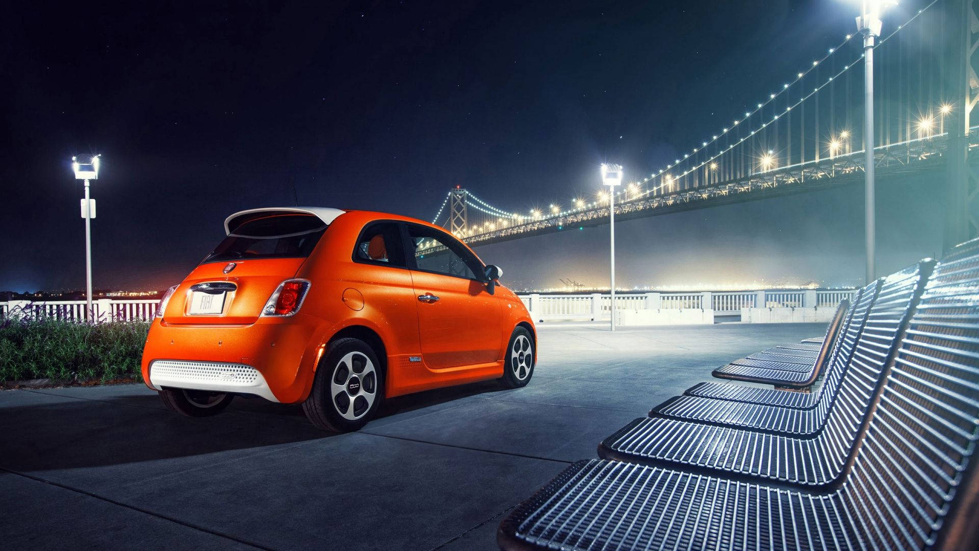 Fiat 桌布 壁紙 — 一輛充滿活力的橙色小型車在夜晚停泊在燈火通明的吊橋下，星空閃爍。
