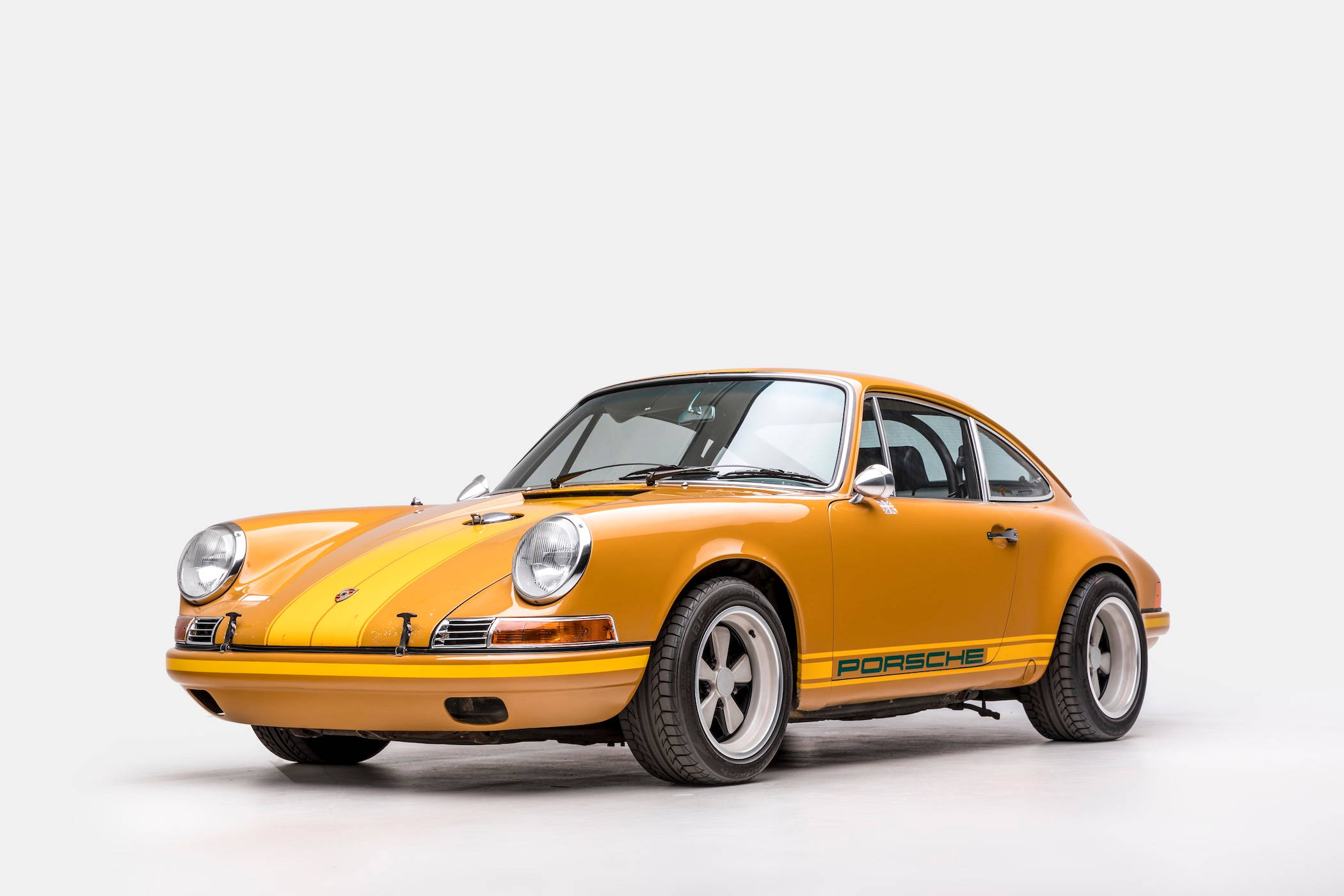 Singer 桌布 壁紙 — 一輛充滿活力的橙色復古保時捷911跑車，帶有黑色賽車條紋和白色側壁輪胎，擺放在乾淨的白色工作室背景前。